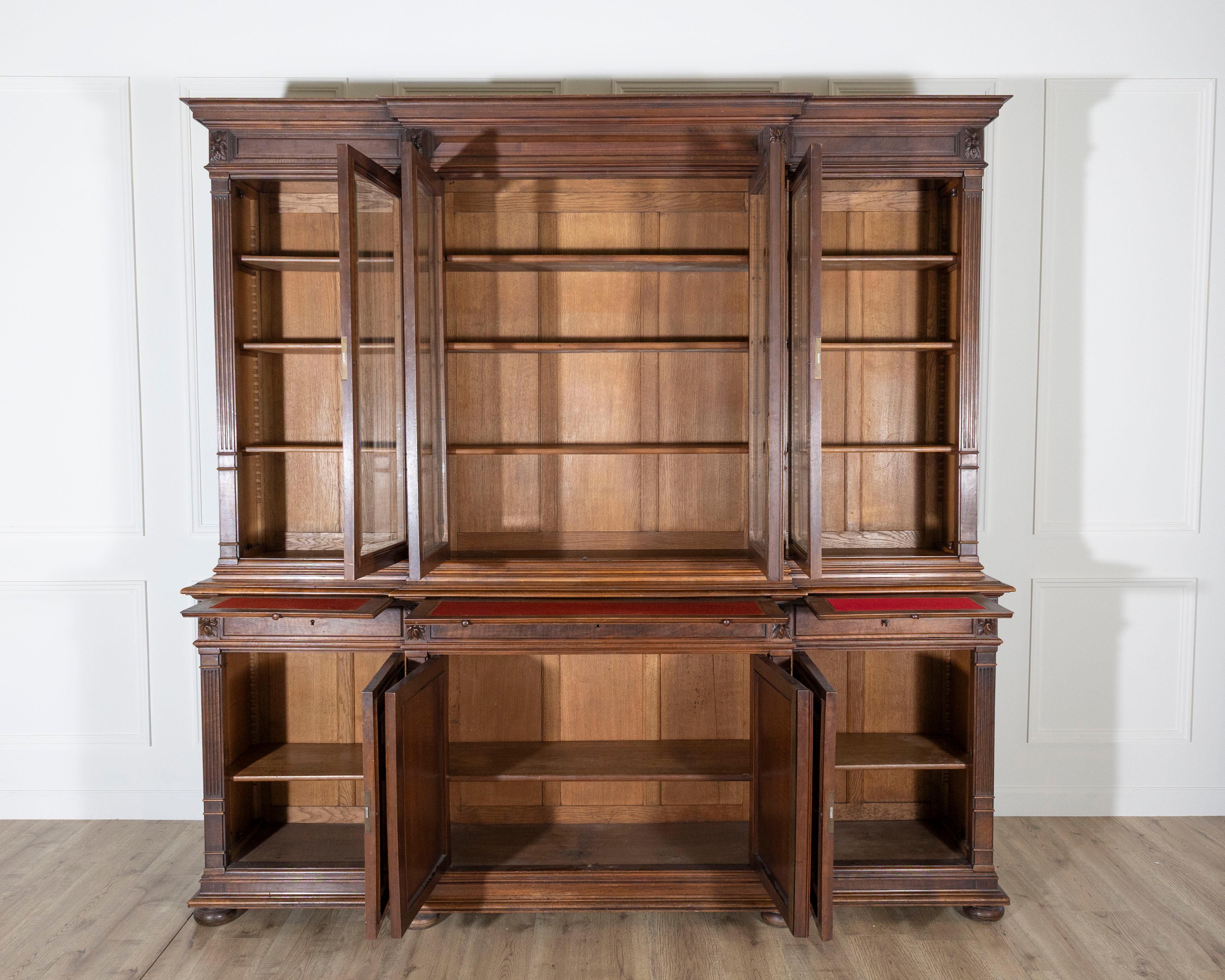 An impressive 19th-century French walnut bookcase in the Louis XVI style, crafted during the Napoleon III period. This monumental bibliothèque is composed of two sections: the upper cabinet showcases four tall glass-paneled doors with beveled glass