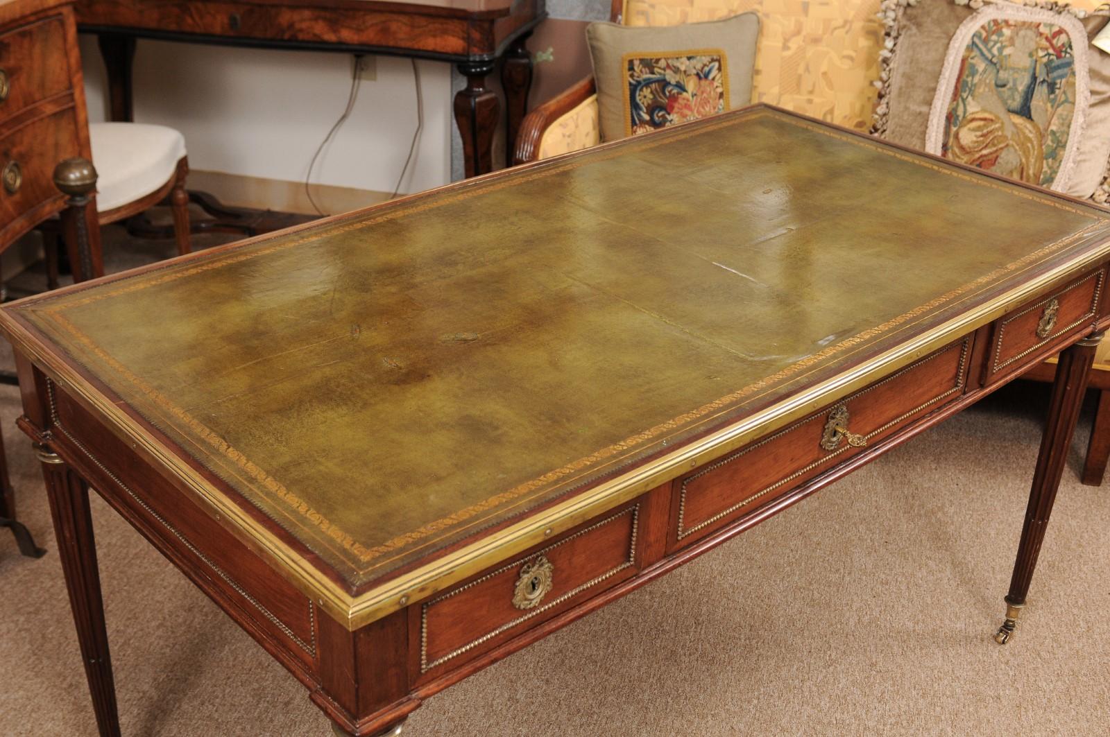 A 19th century French Louis XVI style bureau plat/desk with embossed green leather top, brass mounts, 3 drawers and turned fluted legs ending in caster feet.