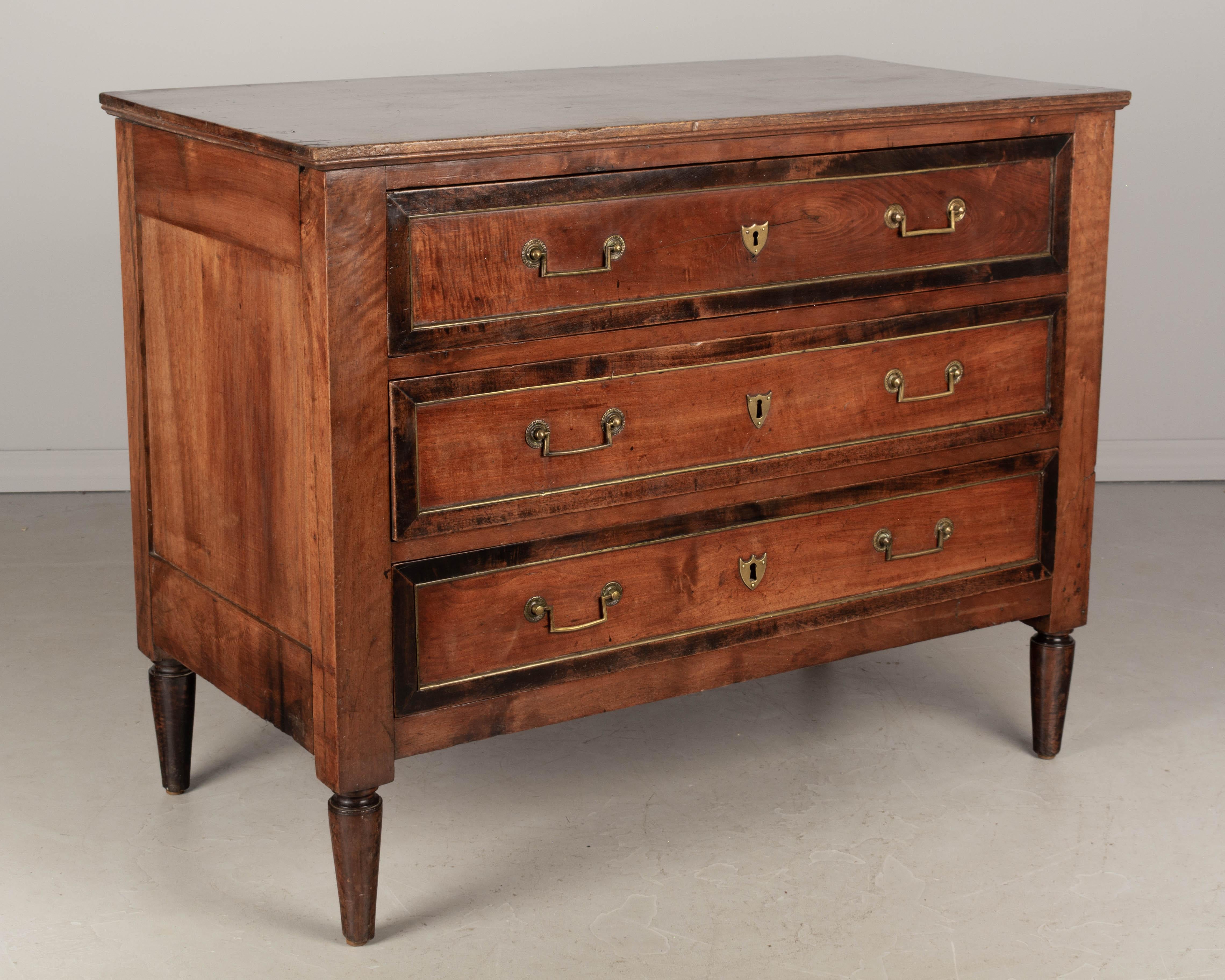 A 19th century Louis XVI style commode, or chest of drawers from the South of France. Made of solid walnut with beautiful patina. Three dovetailed drawers with dark stained outline and brass trim, brass pulls and escutcheons, no locks. Sturdy turned