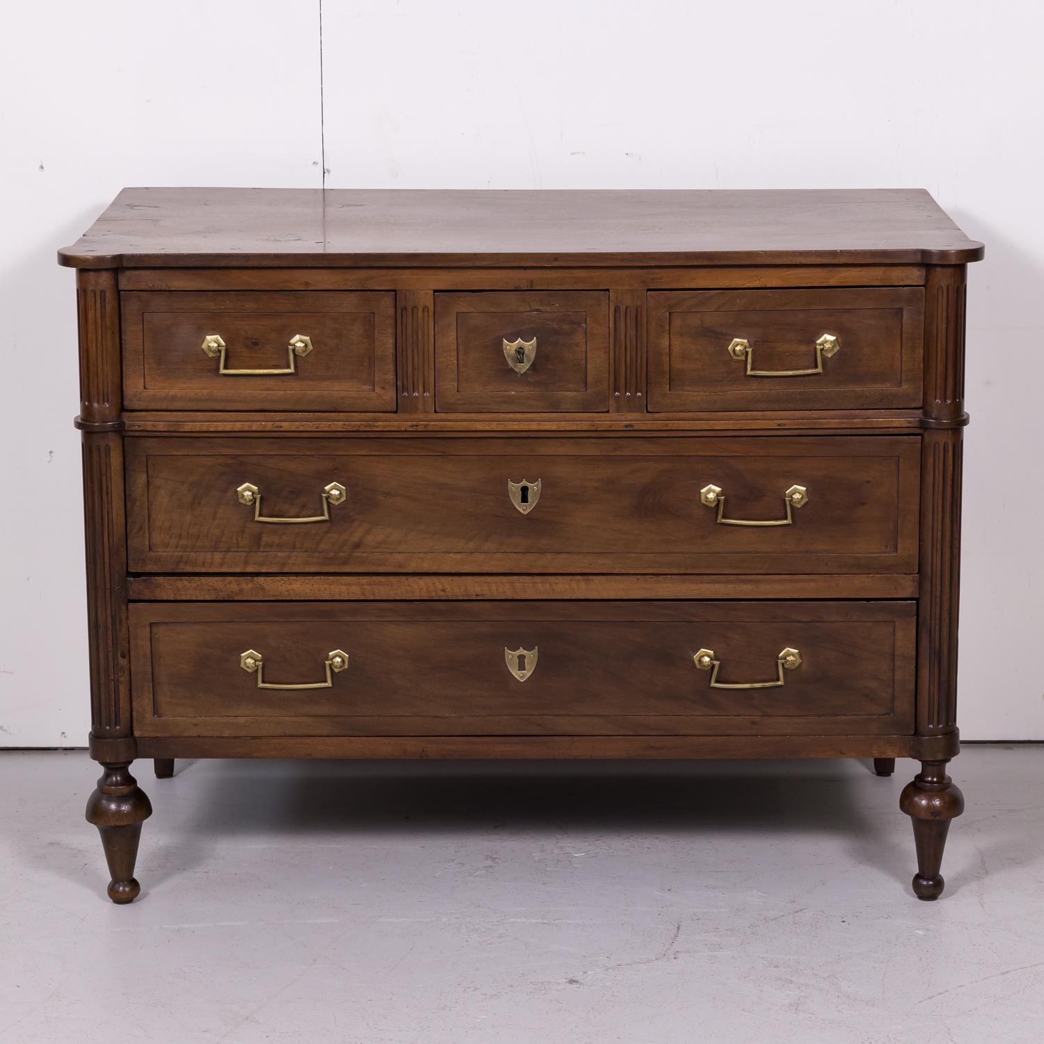 Early 19th century French Louis XVI style five-drawer commode or chest of drawers handcrafted of walnut by skilled craftsmen in Lyon, having original brass hardware, circa 1820s. This handsome commode is supported on curved and fluted stiles sitting