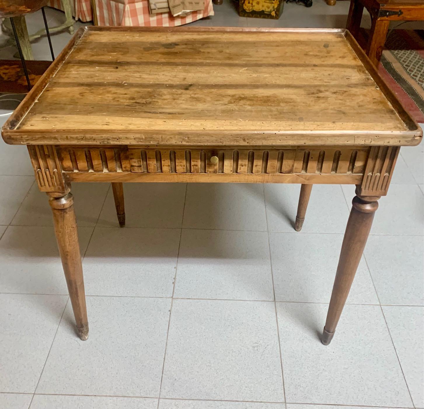 This early 19th century Louis XVI blond walnut side table features hand carvings on all four sides. Its beveled top rests on a fluted apron. from which four long conical turned legs protrude. The table has a single small drawer, it is an ideal table