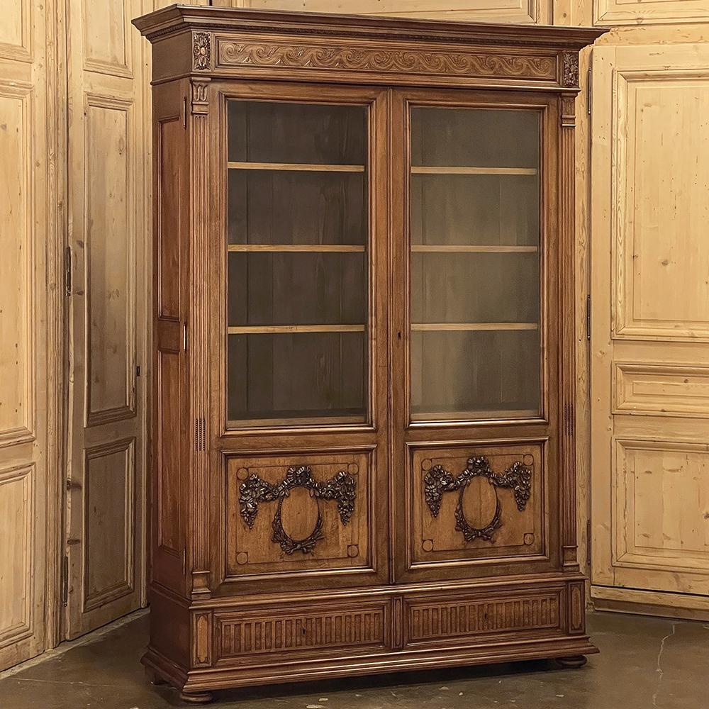 19th Century French Louis XVI Walnut Bookcase represents a stately expression of classical style that truly defies time itself! A multi-tiered crown overlooks the bonnet carved with Greek wave flanked by three dimensional rosettes on each corner,