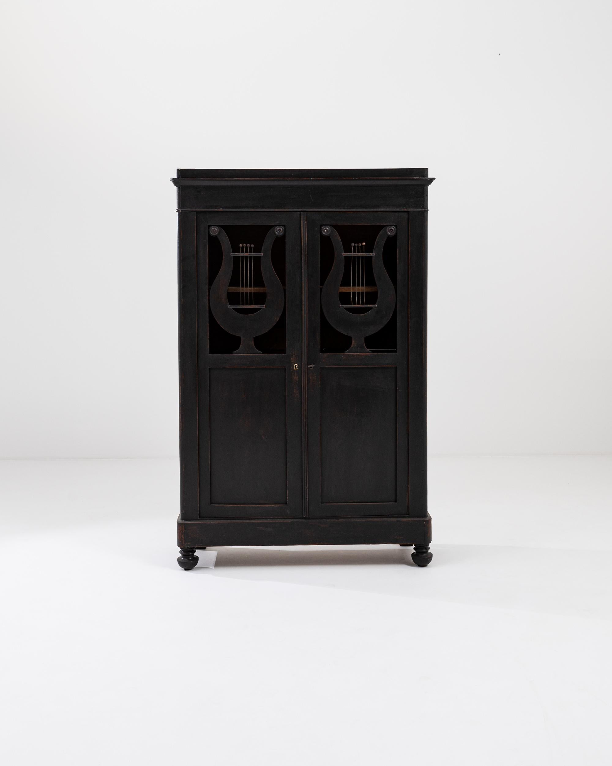 A wooden cabinet from 19th century France. This cabinet is coated in a unique, mature patina; black paint lets a russet oak tone shine through at its edges. Two doors swing outwards revealing four storage shelves, whose natural wood tone compliments