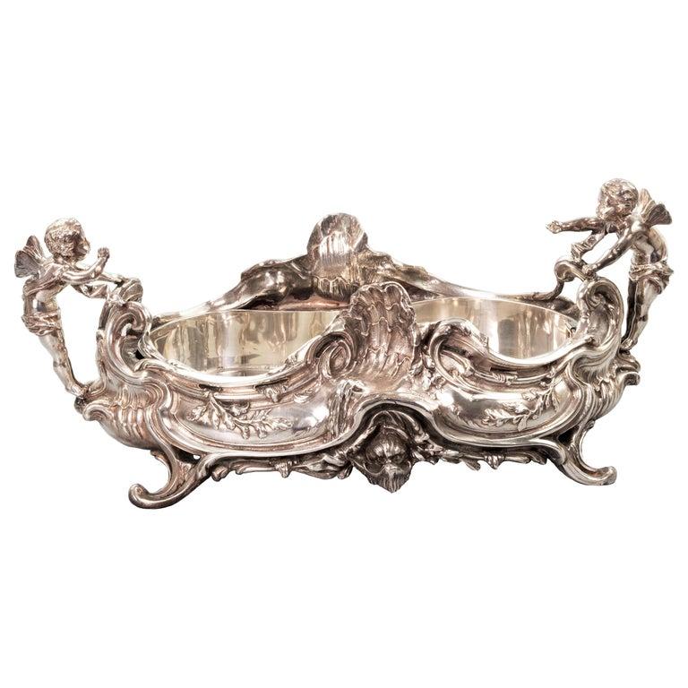 This massive silver plated centerpiece is modeled in “Rococo” style, with its famous “C” and “S” scrolls. Two putti on both side of the handle enlivens the whole piece as they were exchanging conversion over the dining table.
The piece sits on a
