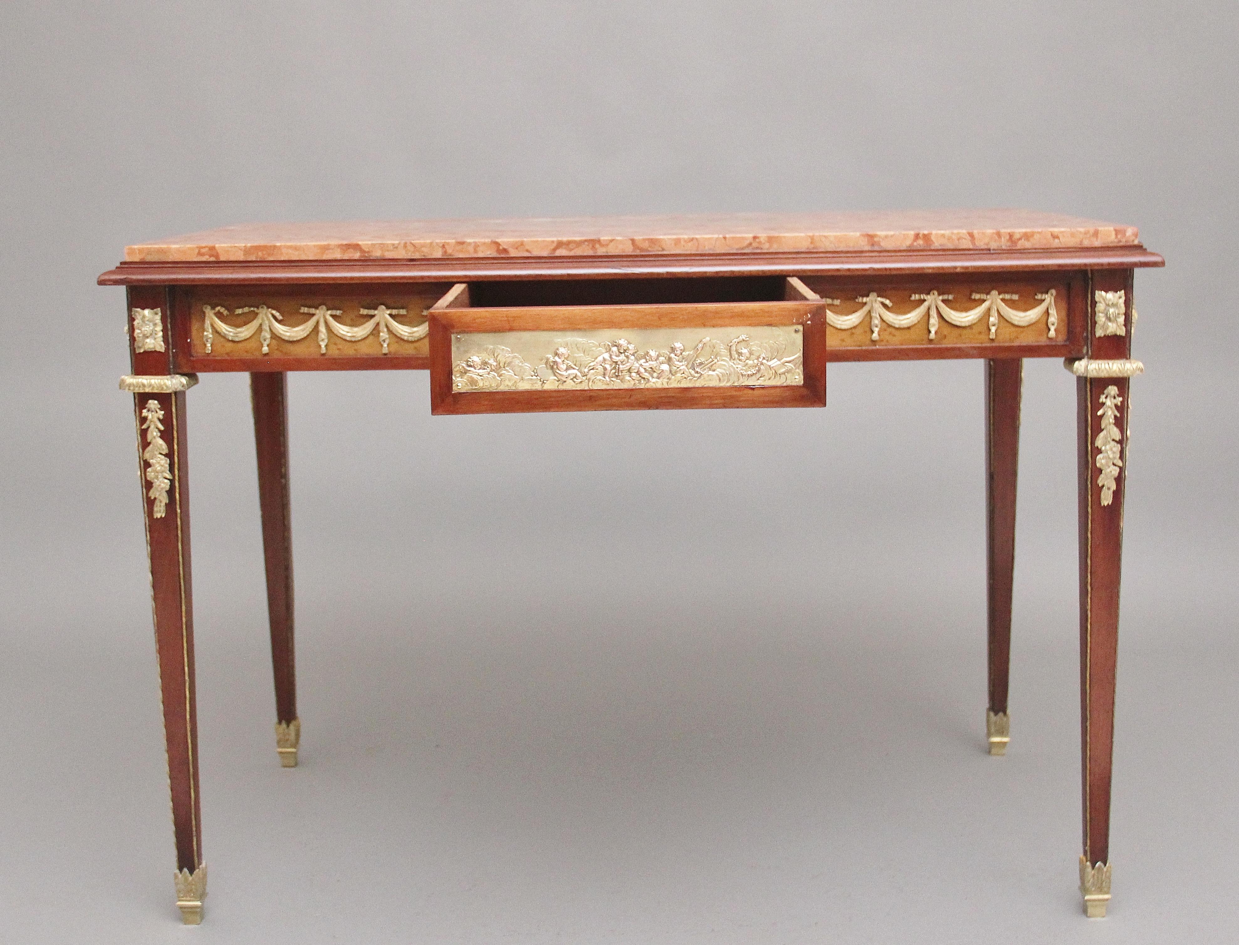 19th Century French mahogany and marble top centre / occasional table in the manor of Francois Linke (1855 – 1946) having the original inset rouge marble top, with a single oak lined frieze drawer below with a decorative brass plaque with cherubs