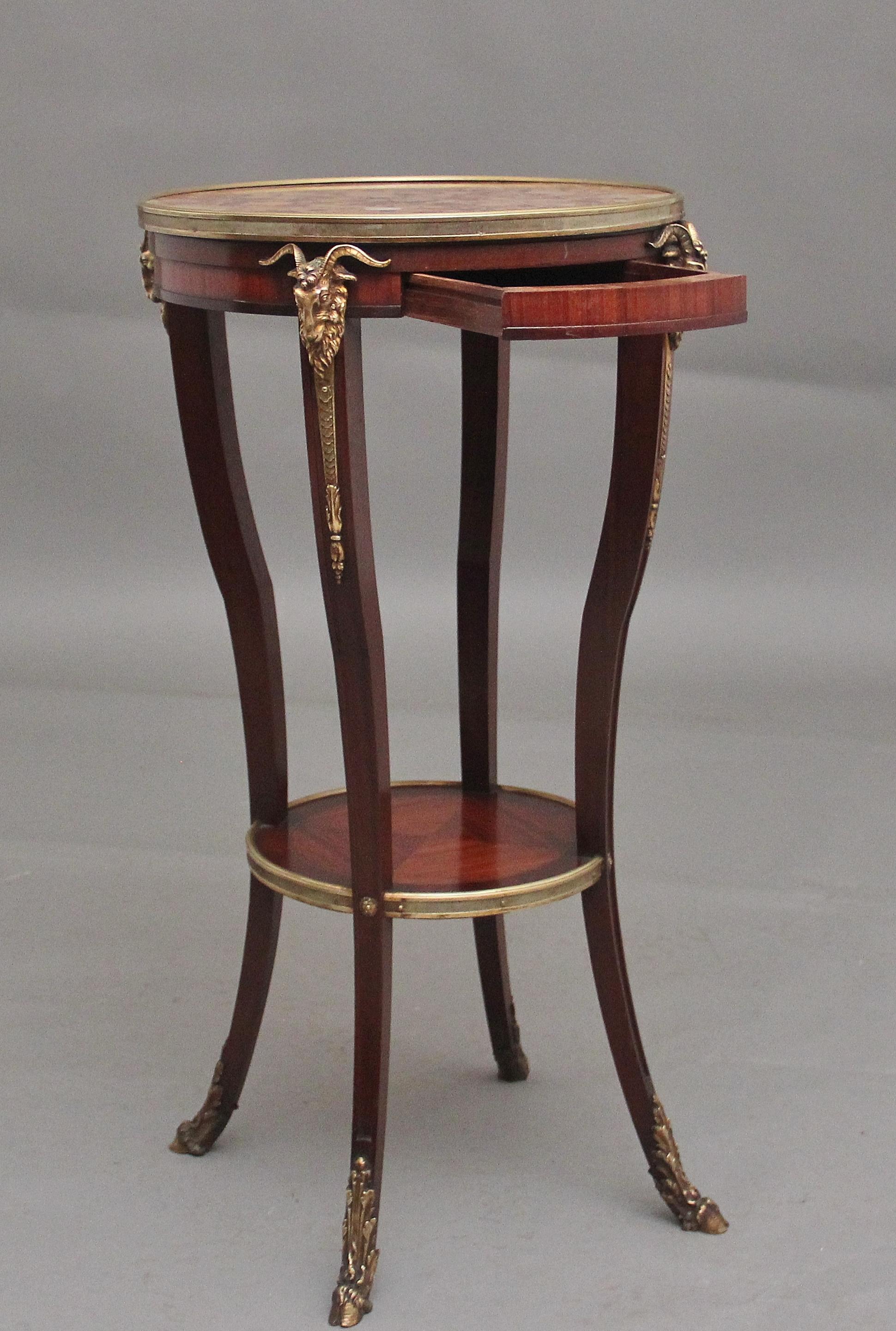 19th Century French mahogany and marble top occasional table, the circular speckled rouge marble top having a brass moulded edge, having a single frieze drawer below with four decorative brass rams heads above each support structure leading down to
