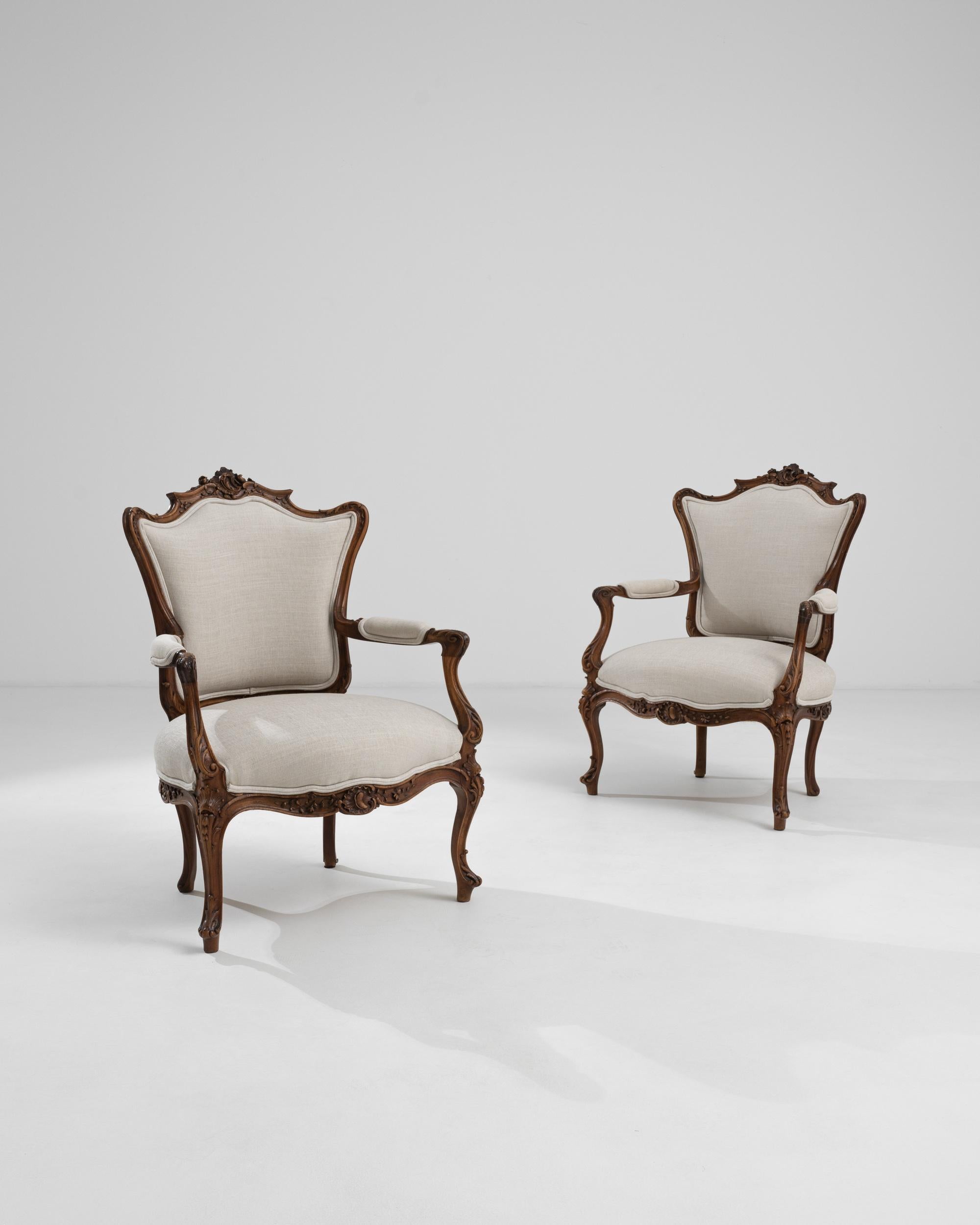 A pair of 19th century French wooden armchairs with upholstered seats and backs. A warm and pleasing glow emits from the rich brown wood that composes these elegant chairs. Sumptuous carved scroll patterning is given revitalized synergy thanks to