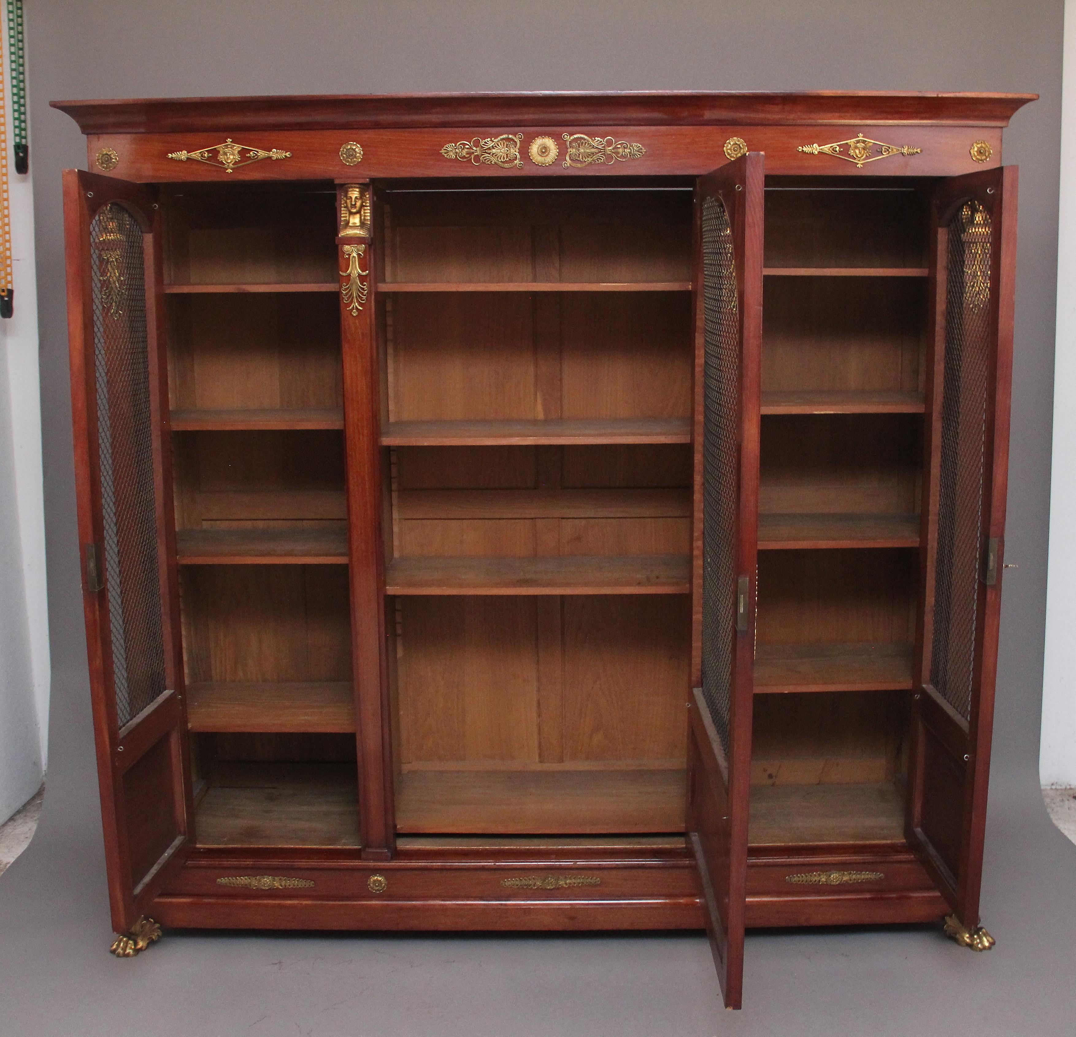 A superb quality 19th Century French mahogany bookcase in the empire style, the shaped cornice above three moulded arched doors with wire grills opening to reveal four adjustable shelves in each section, each door front having a panel at the bottom