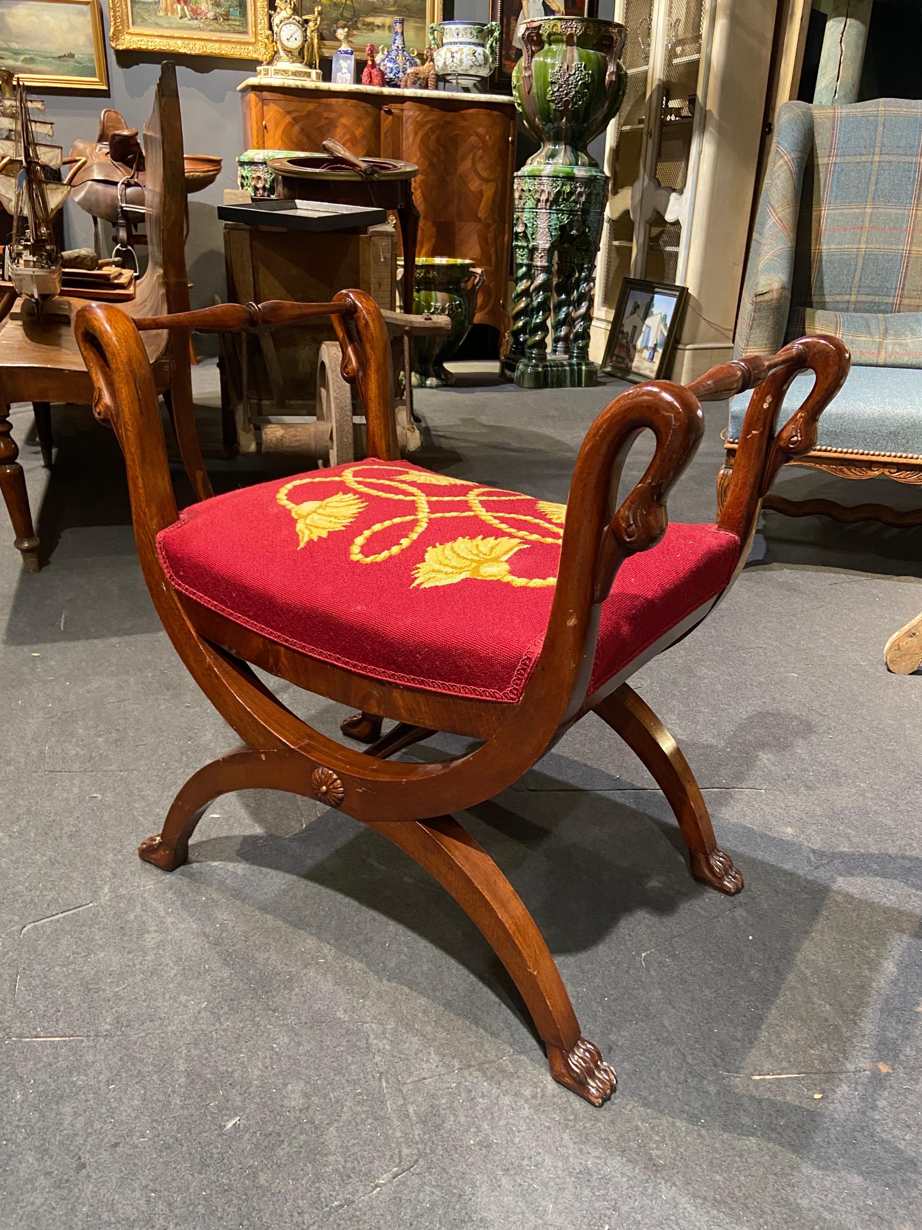 Elegant French mahogany hand carved curule stool with four swan's heads decorating the armrests. It is made in Empire style and is with the original upholstery in red and yellow in quite good condition. The stool is very stable and