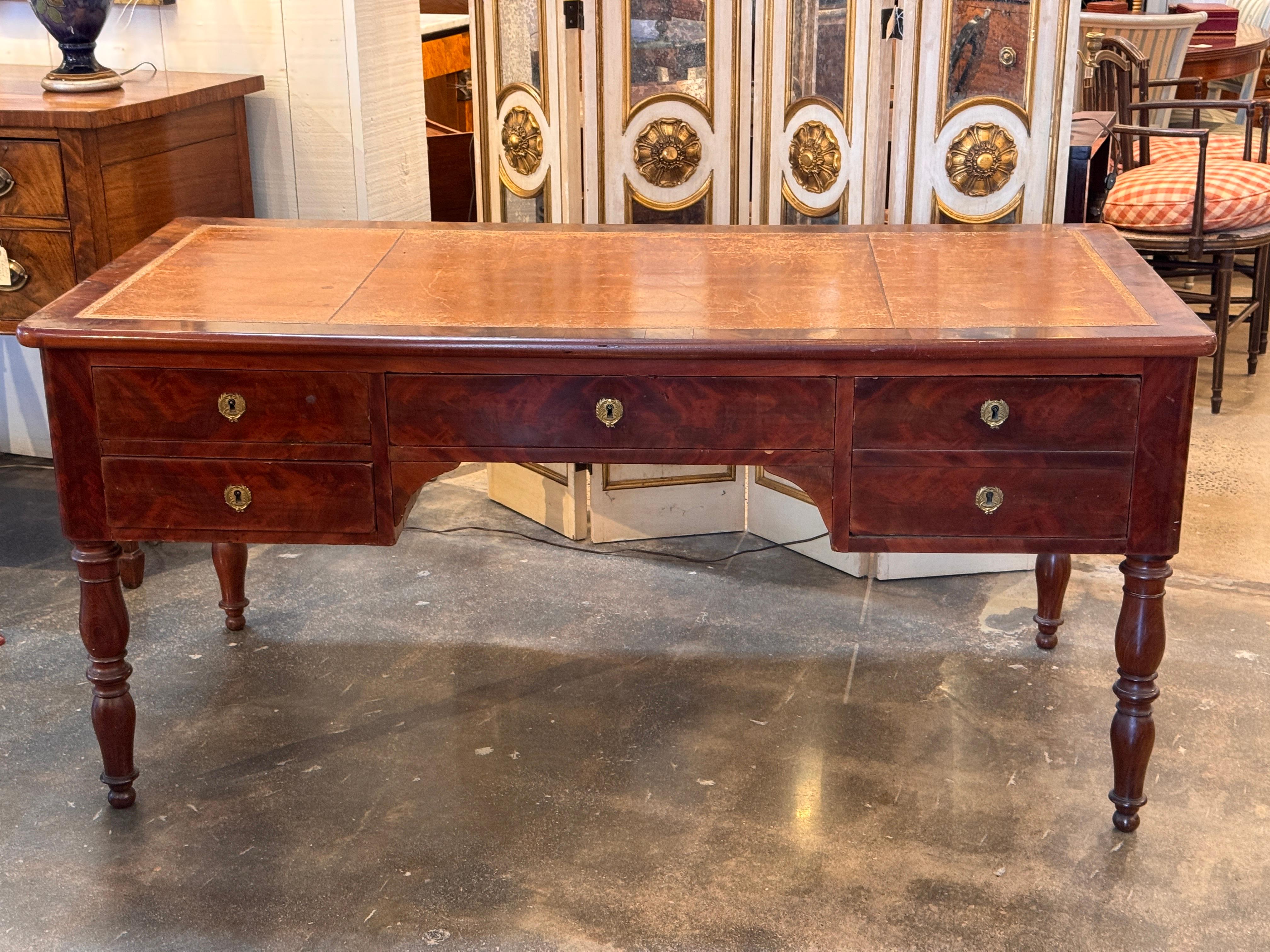 French mahogany desk with a tooled leather writing surface and slide extensions at each end. The case features a shaped kneehole and six drawers with period-style brass escutcheons. Turned legs support the rectangular top, and the leather panels