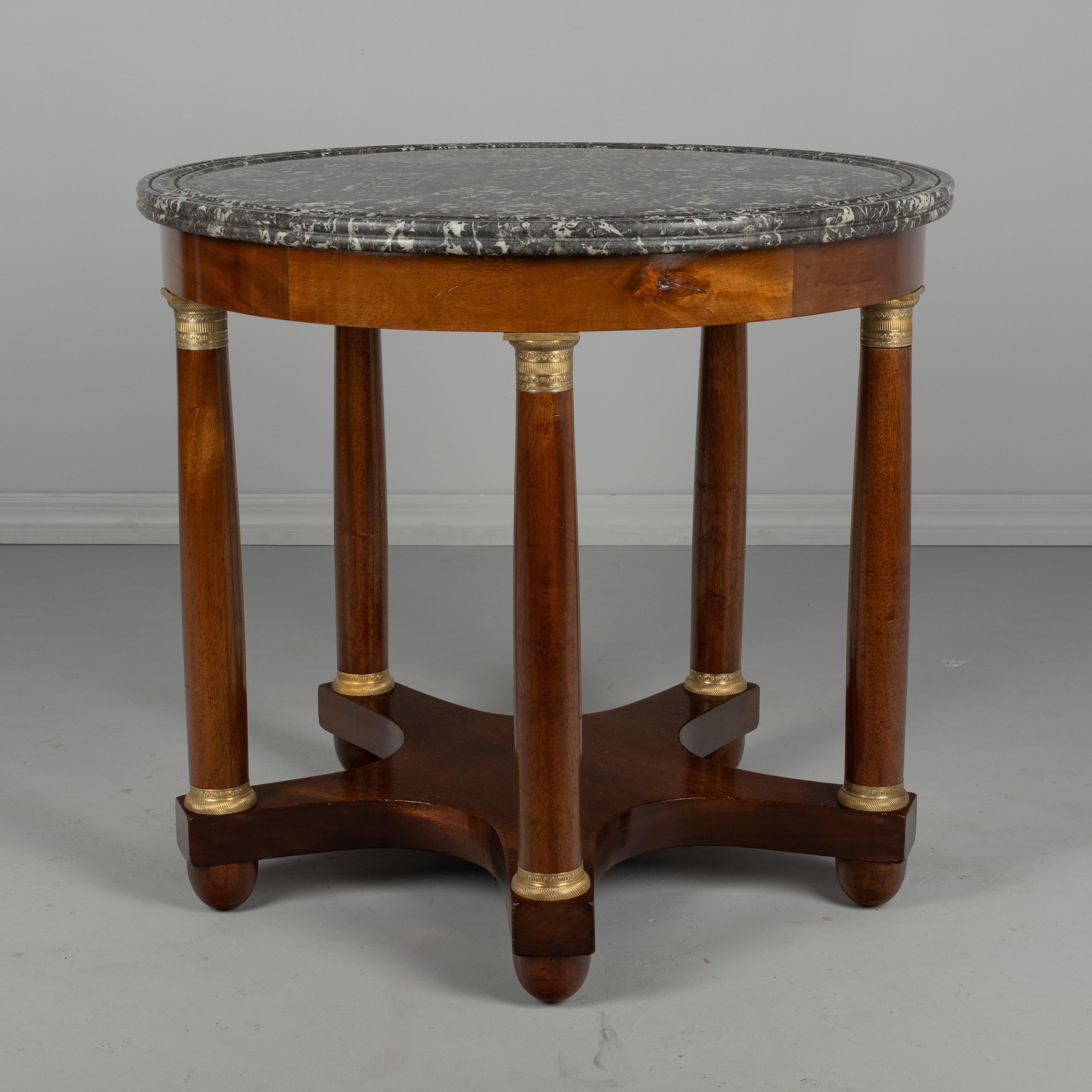 A fine 19th century French Empire style gueridon or center table made of solid mahogany with veneer of mahogany banding around the top. Five bronze mounted legs on a curved base with bun feet. Grey St. Anne marble top with double grooves. French