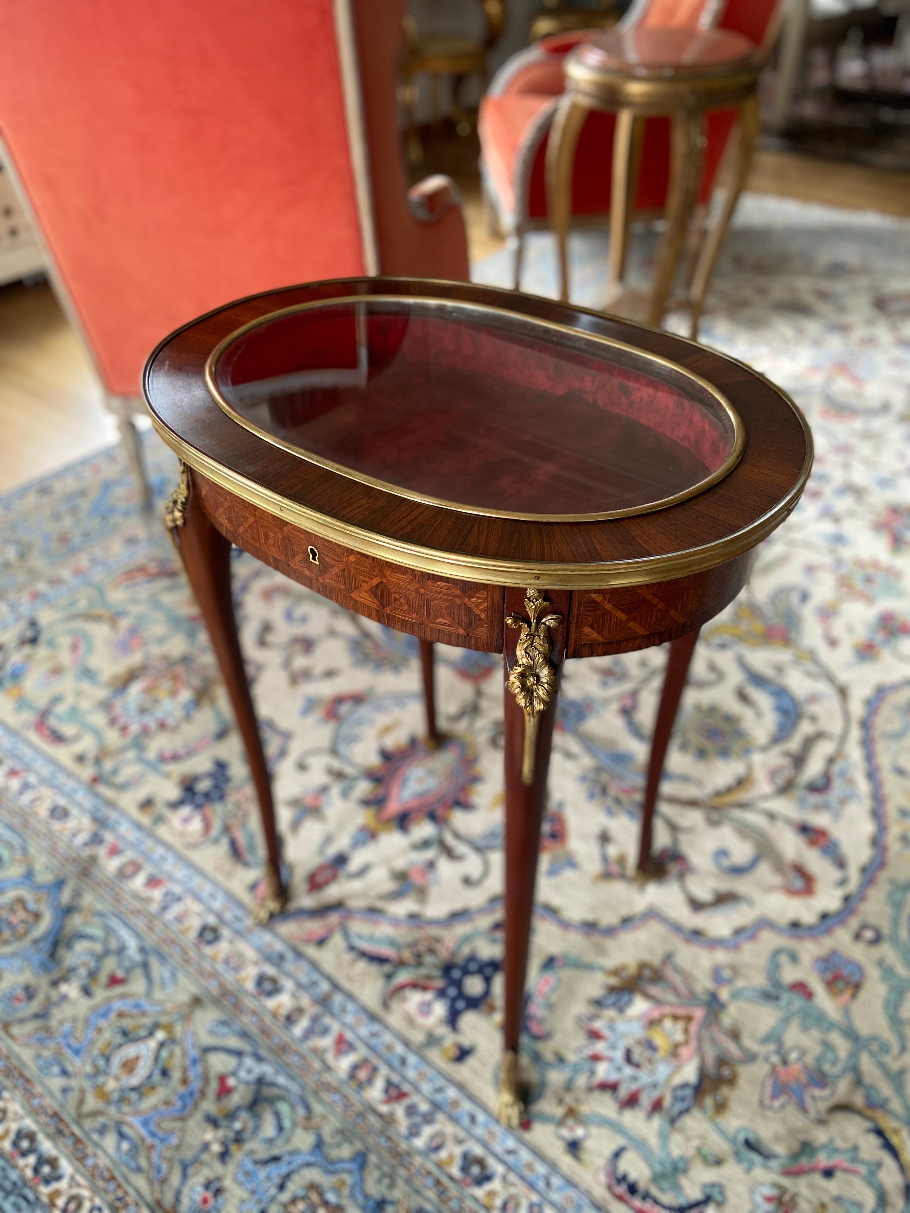 A fine quality French late 19th century mahogany hand carved inlaid oval table bijouterie cabinet in Louis XVI style. The glass top opening to access the red velvet interior. Raised on four elegant cabriole legs, each one ending with bronze paw.