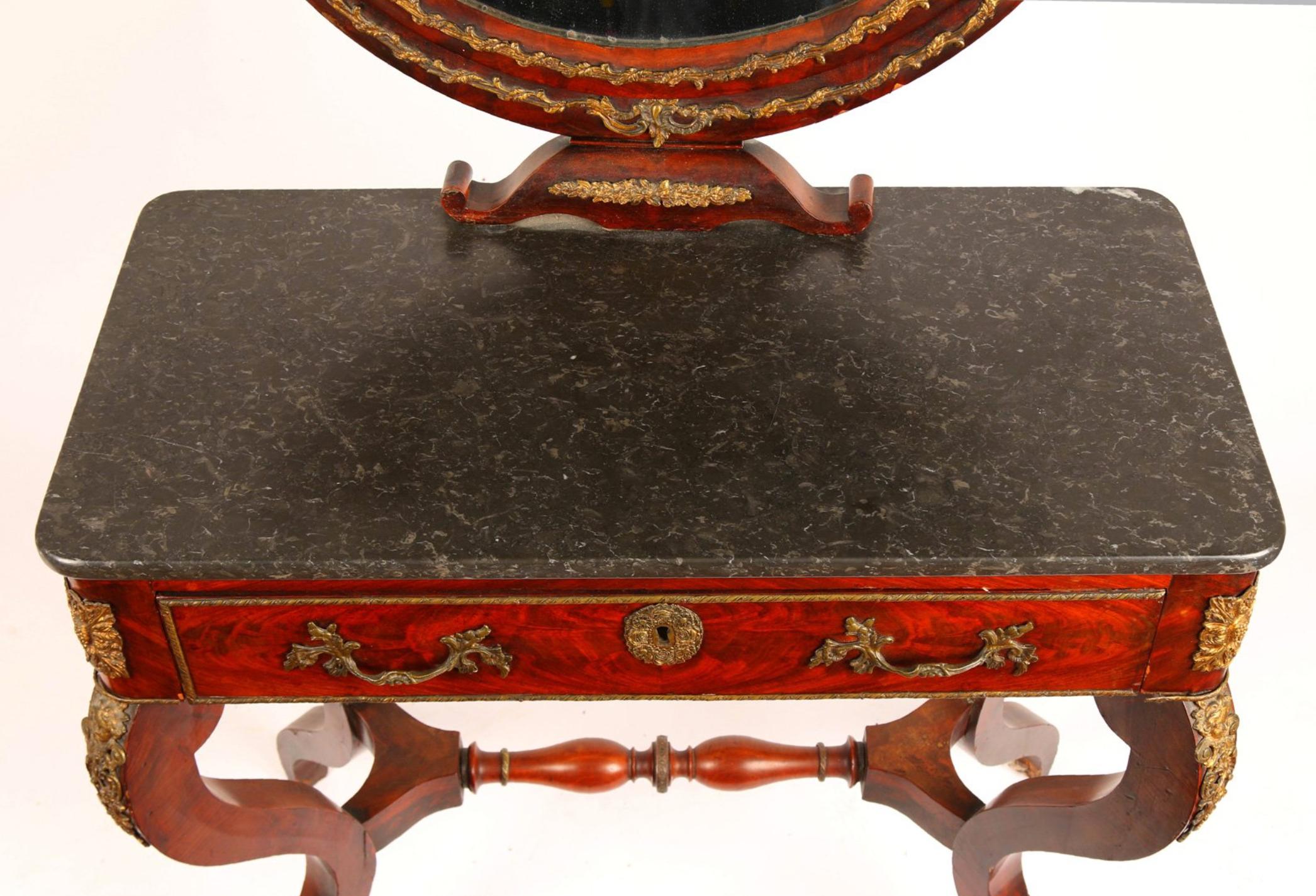 French hand carved mahogany vanity table with black marble top. There is an original crystal oval mirror on the top part surrounded by two asymmetrical swan's heads. The piece is raised on stable cross legs connected in between. There is one large