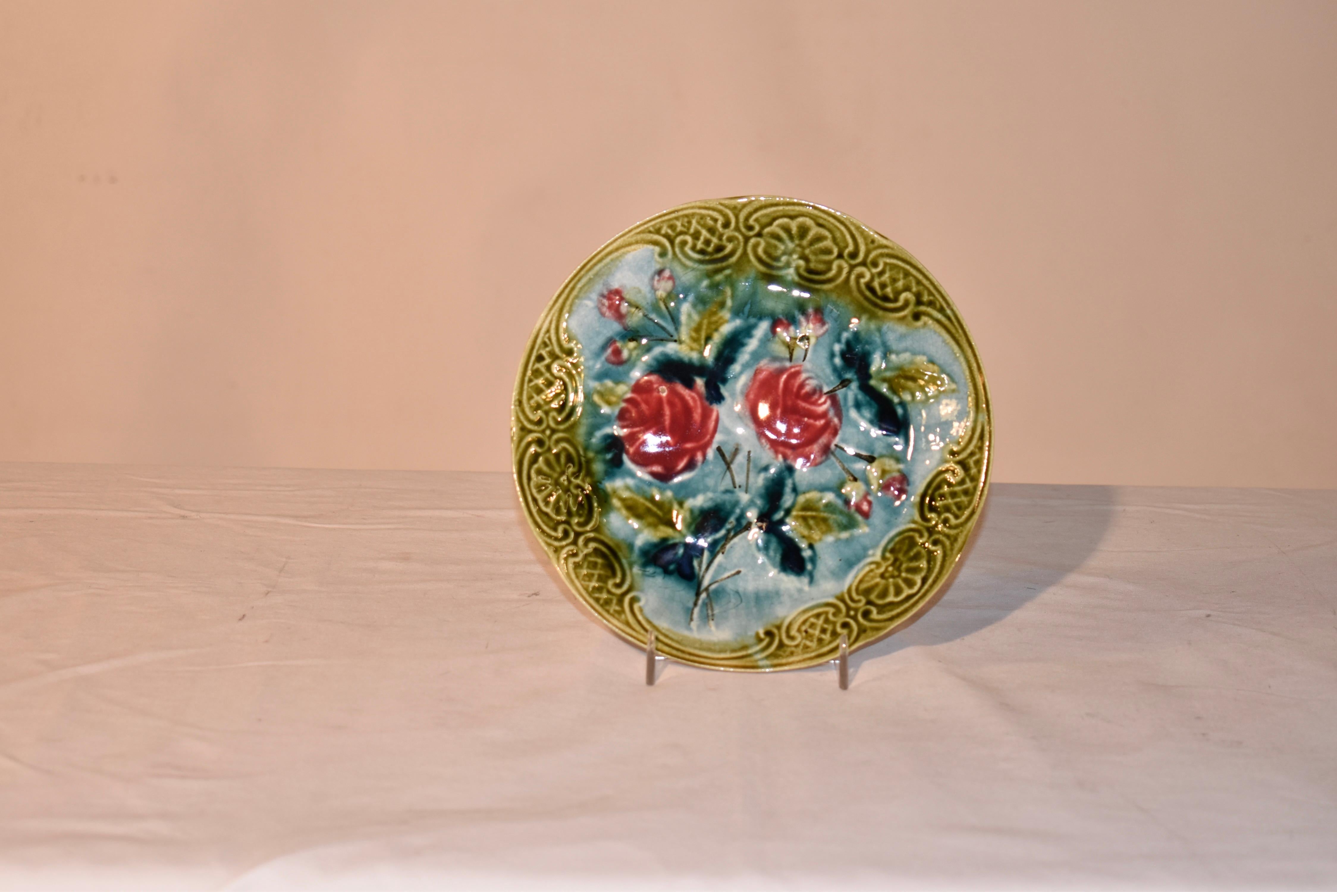 Assiette en majolique française de la fin du 19e siècle, avec une jolie bordure à volutes et un motif central de superbes roses et boutons de rose avec des feuilles.  Le support n'est pas inclus.
