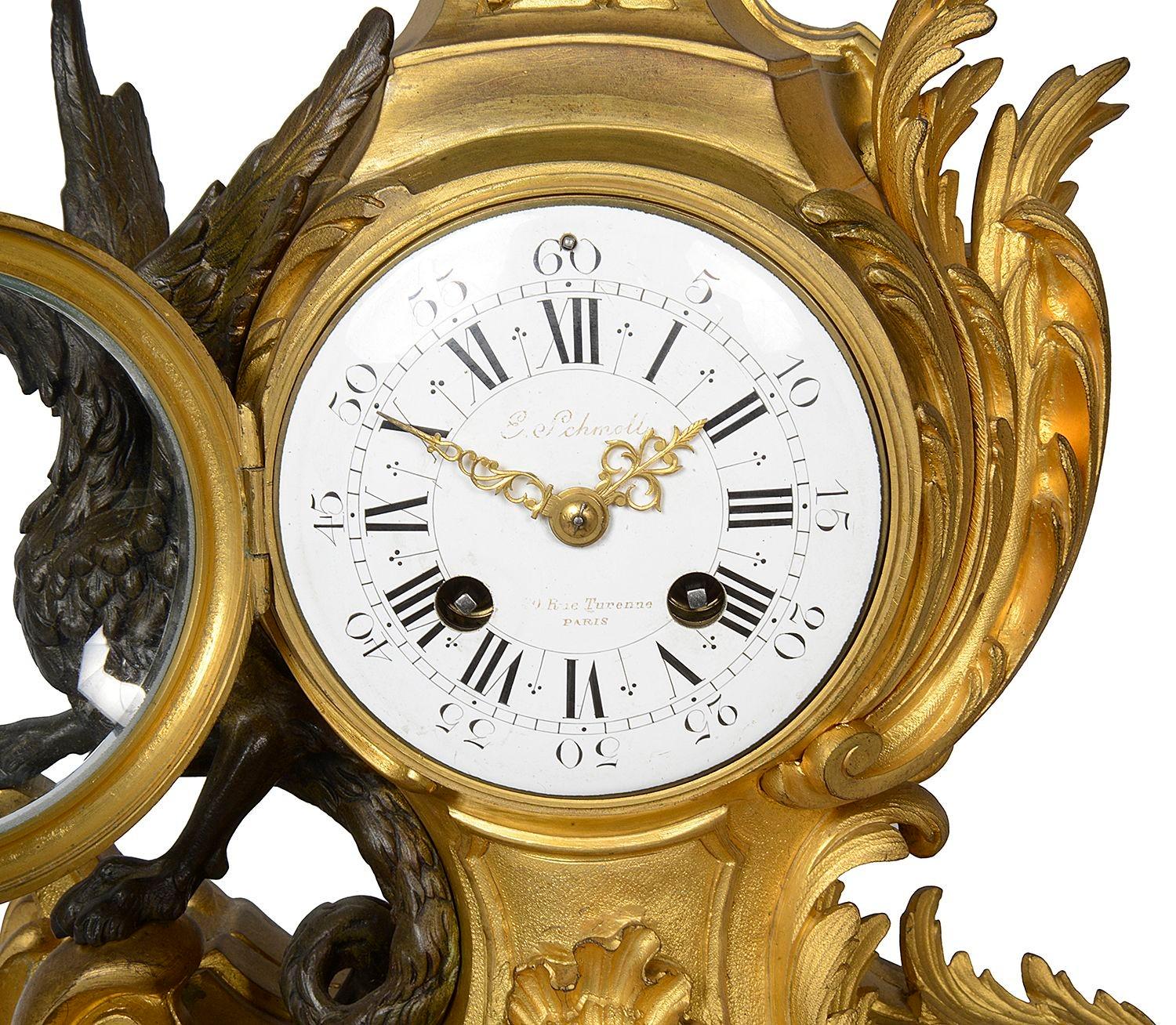 A very good quality late 19th Century French gilded ormolu and patinated bronze mantel clock, having a seated cherub holding the rains of a winged dragon pulling a scrolling foliate rococo style chariot. The white enamel clock face with roman