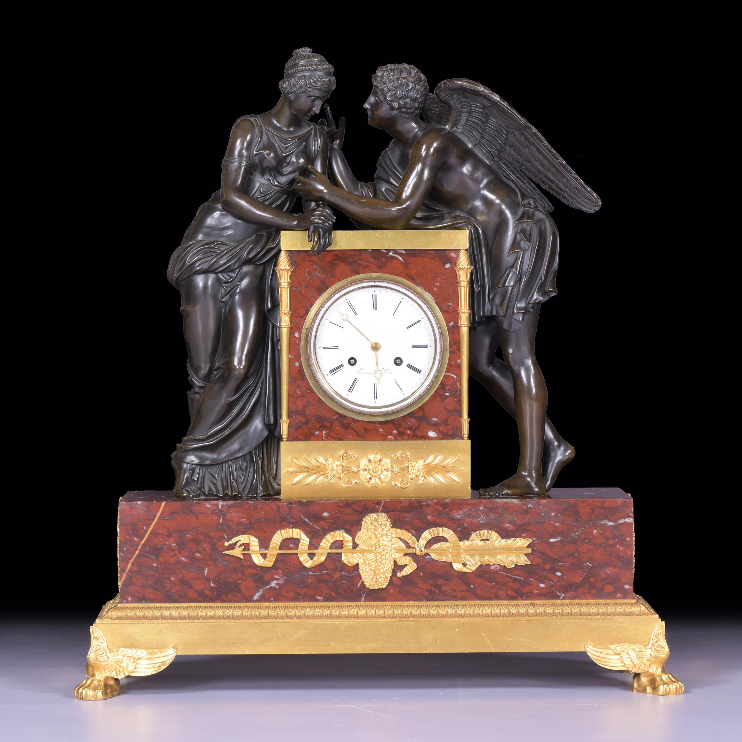 An exceptional early 19th century rouge marble, bronze and ormolu mounted neo-classical mantle clock depicting Psyche and Cupid. The 4 1/2 inch white enamel dial is signed Caron a Paris and flanked by two flaming torches of ormolu The base has an