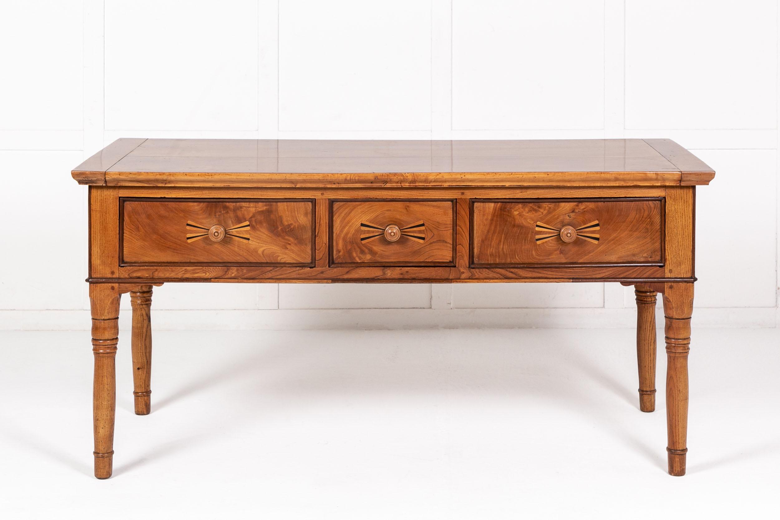 19th Century French maple and elm table. Having a two plank top with cleated ends. Three deep drawers below with central ribbon effect, of ebonised and elm wood inlay, with turned wooden pull handles. The whole is raised on turned