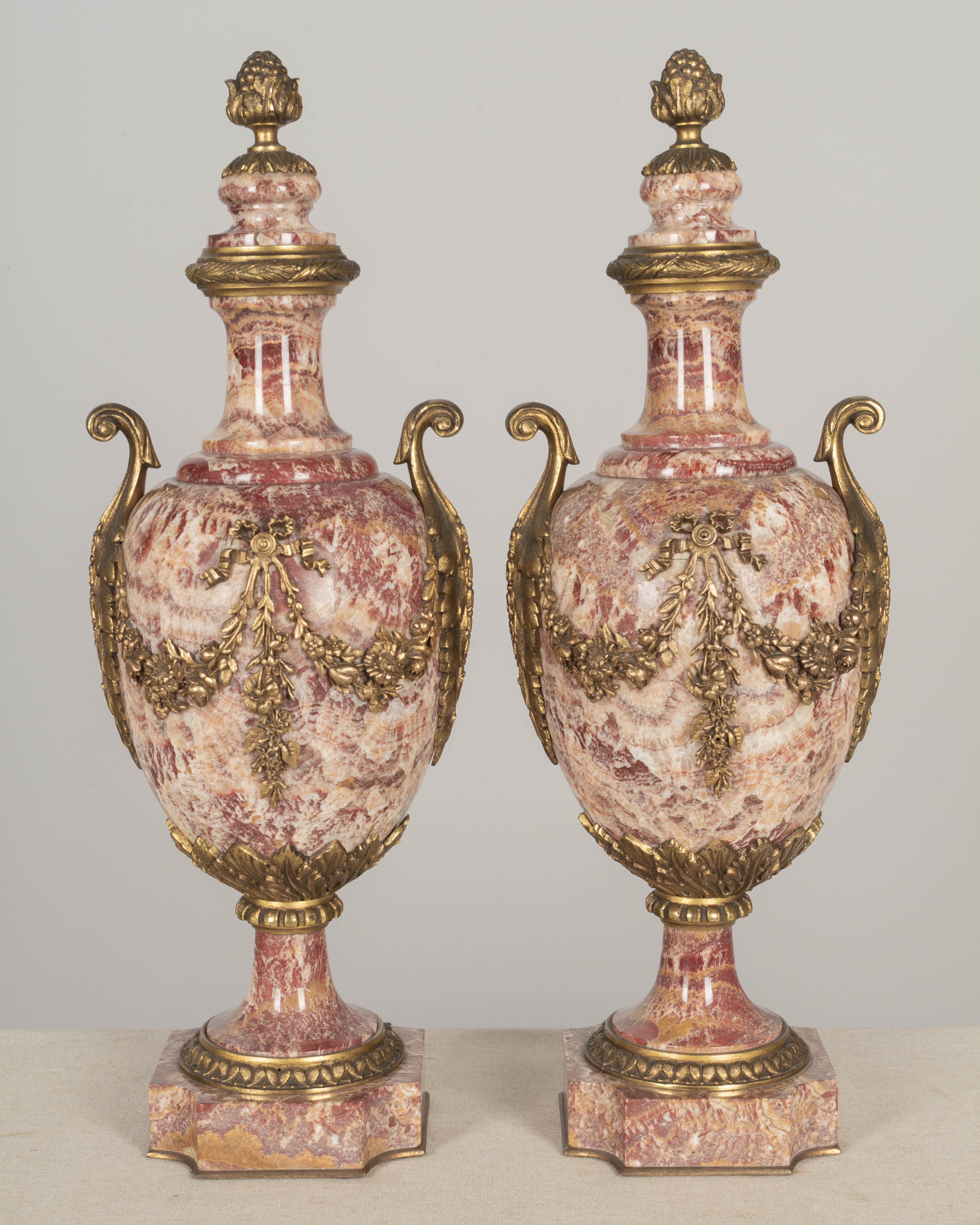 A pair of 19th century French bronze mounted urn form cassolettes with beautiful deep red and orange veined polished marble. Nicely detailed cast floral garlands, and large foliate handles. Attached lids with acorn finials. Small chip to the lid of