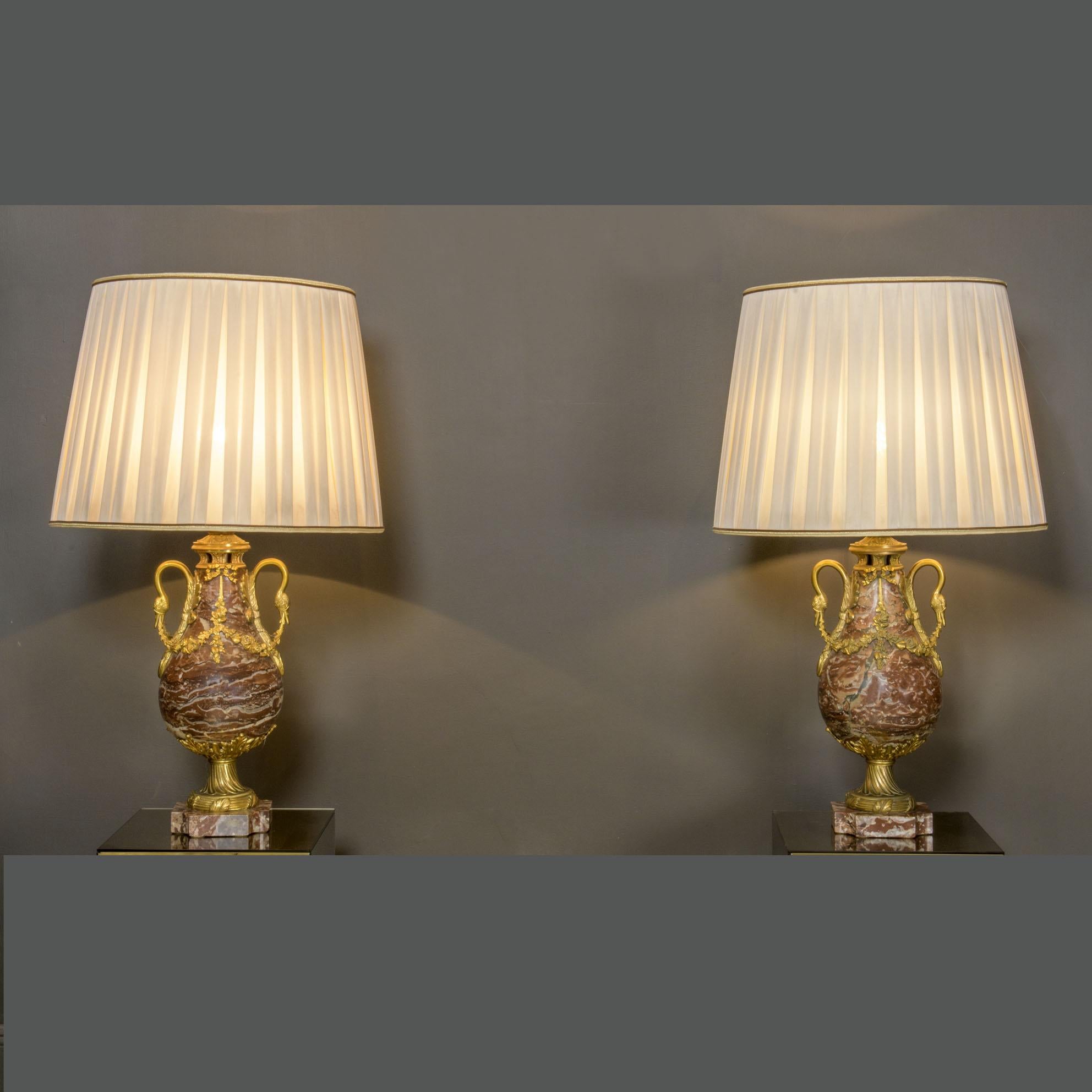 Paire de vases en marbre et en bronze du XIXe siècle, transformés en lampes dans le style Louis XVI. 
Ils présentent d'importantes décorations en bronze doré : bandes florales, bordures de feuilles, rubans et cygnes gracieux en guise de poignées.