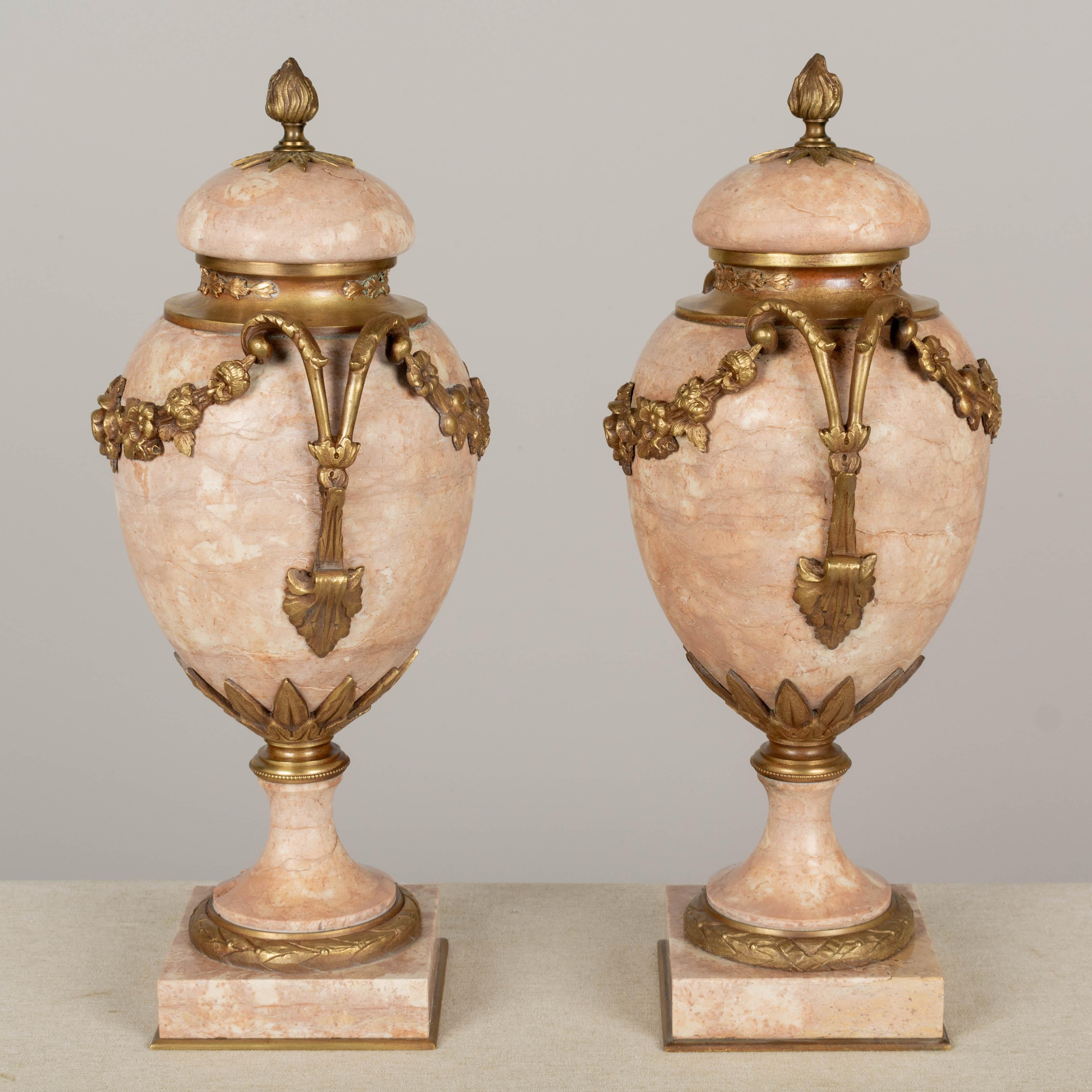 A pair of 19th century French bronze mounted urn form cassolettes with beautiful rose colored marble and nicely detailed cast floral garlands. Removable lids with flame finials. Small chip to the base of one pedestal. circa 1880-1900. 
Dimensions: