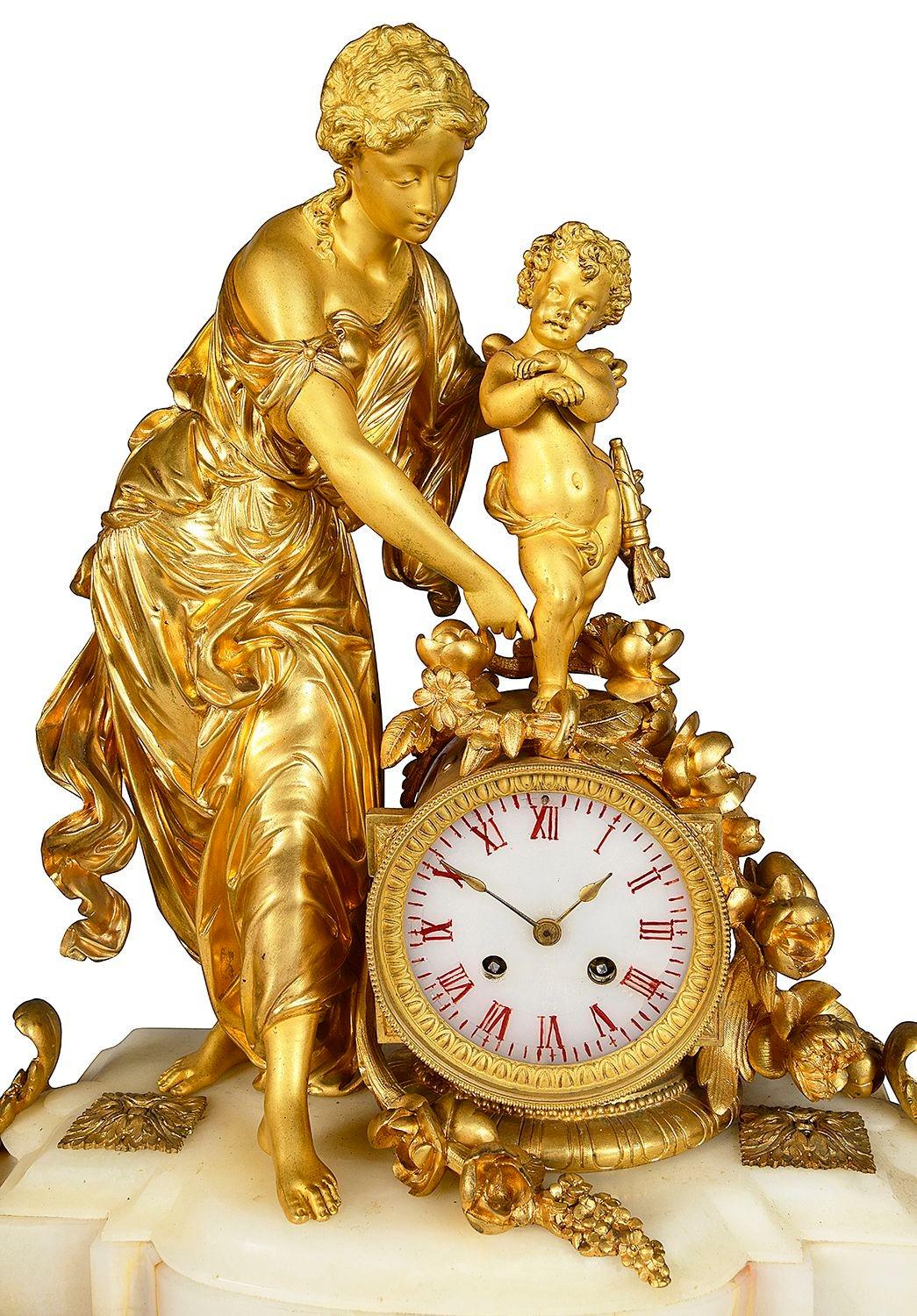 An enchanting French 19th Century white marble and gilded ormolu clock garniture, having a mother and childly the white enamel clock face, striking on the hour and half hour on a bell. Raised on a marble base with ormolu feet. Either side a pair of