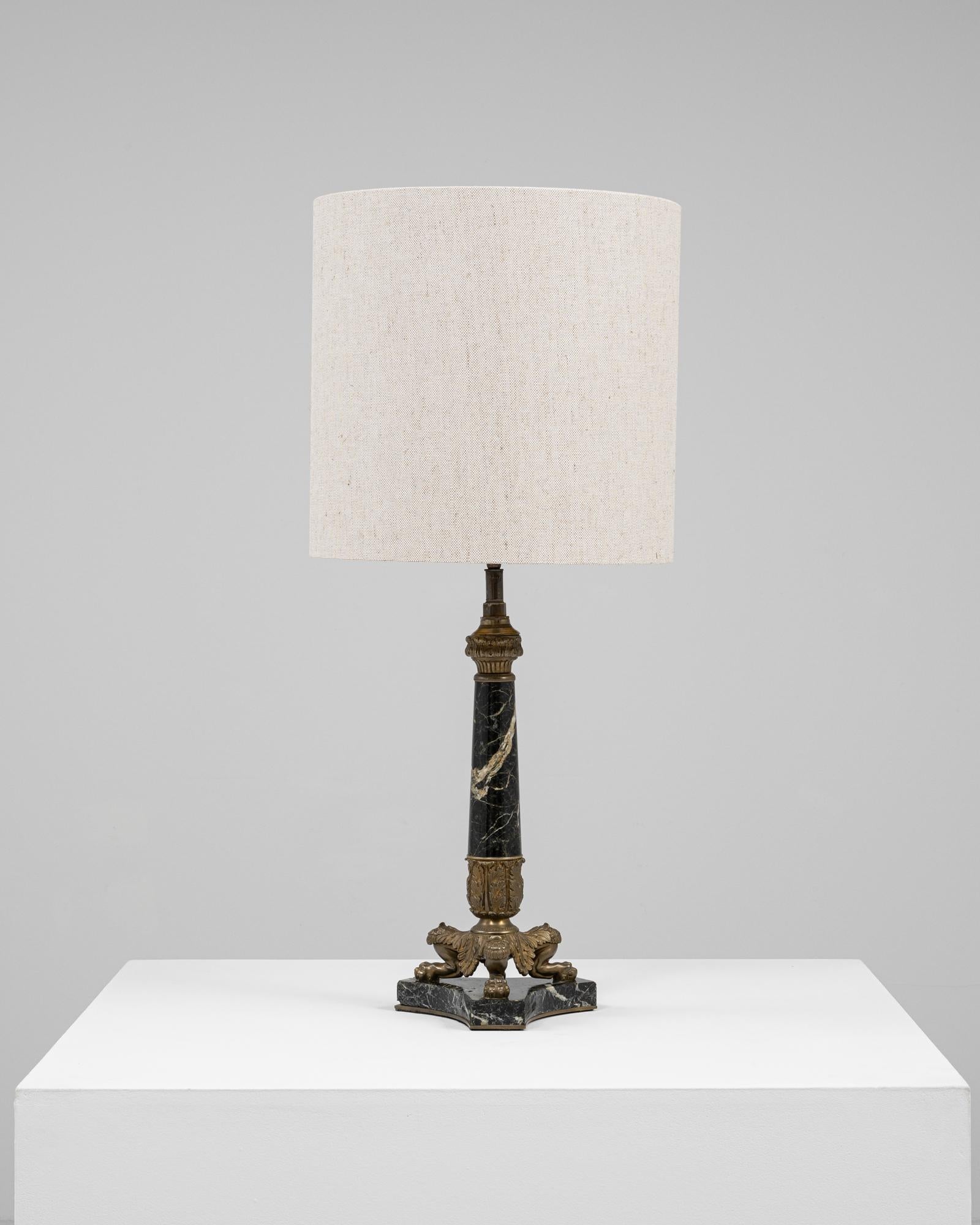 Esta lámpara de mesa francesa del siglo XIX es una refinada composición de mármol oscuro y latón ornamentado, que combina la elegancia clásica con el detalle escultórico. La columna cónica de mármol está veteada con vetas doradas naturales, creando