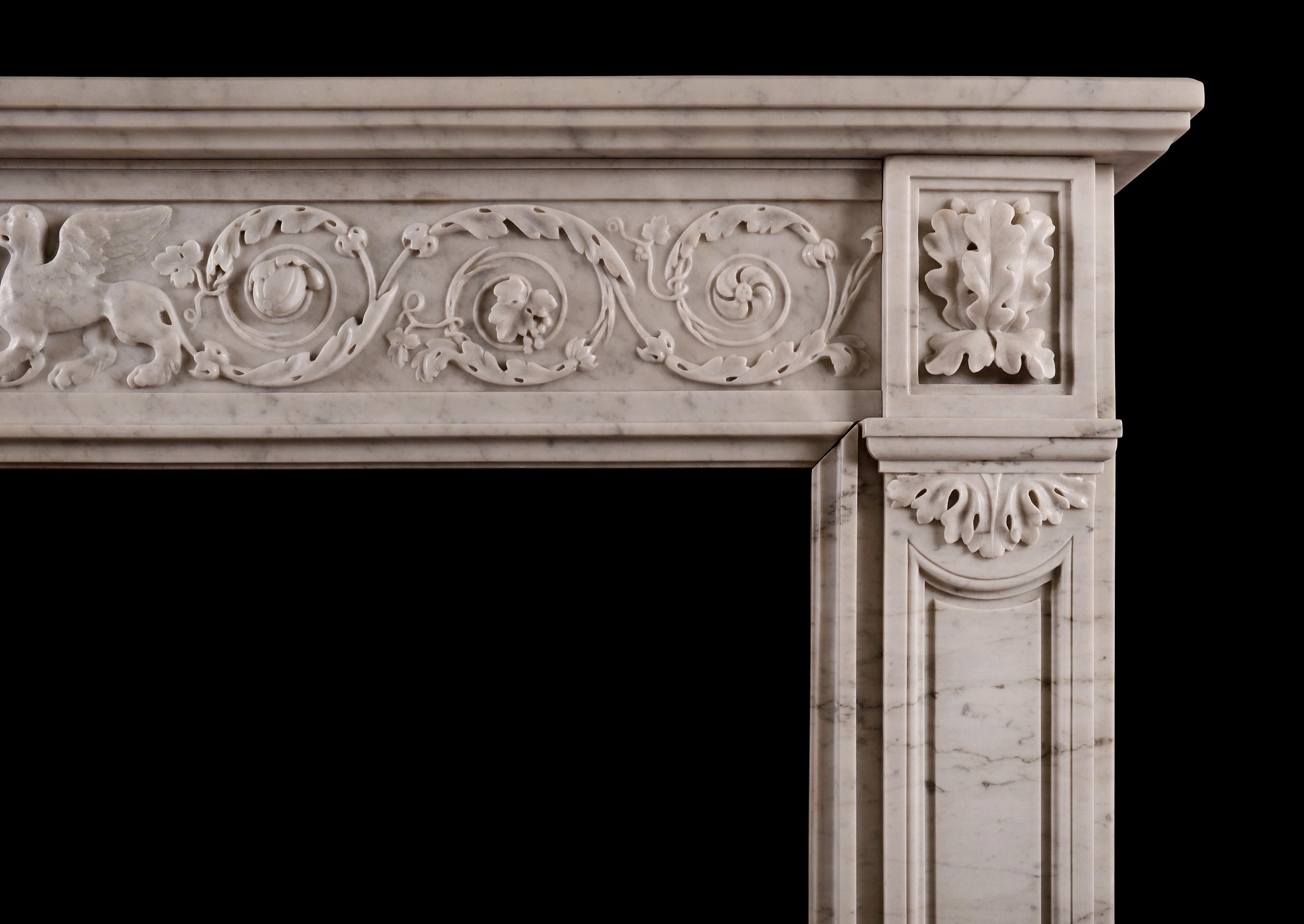 Une cheminée française de style Louis XVI en marbre de Carrare. La frise est ornée de feuillages sculptés et de pateras tourbillonnants, avec des bêtes ailées et une urne au centre. Les montants avec panneau façonné sont surmontés de blocs