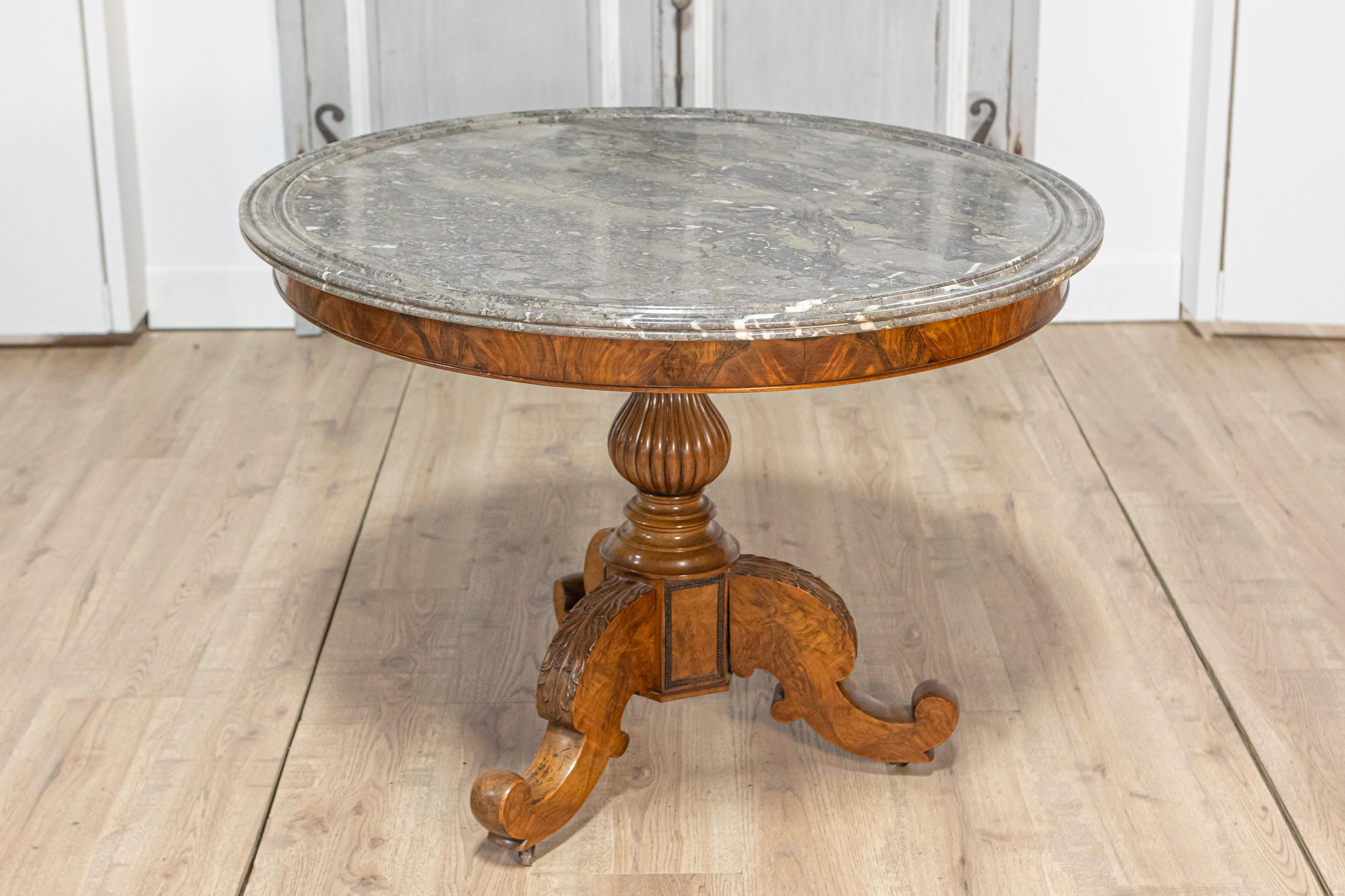 Esta llamativa mesa central francesa del siglo XIX es un testimonio de la elegancia y la artesanía de la época. Con un lujoso tablero redondo de mármol, la mesa muestra una piedra gris y blanca bellamente veteada, enmarcada con un borde