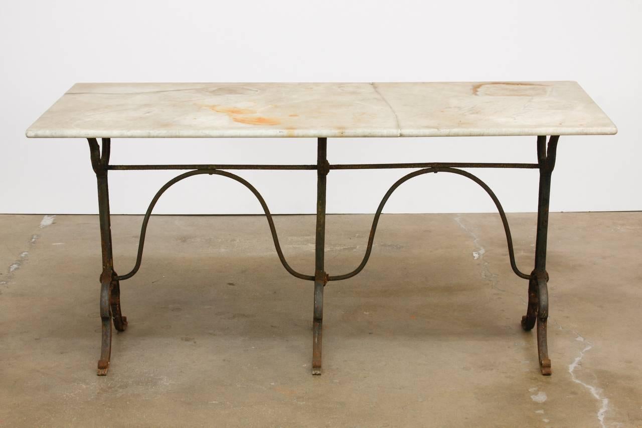 Rustic 19th century French pastry table, bistro table or console table featuring a weathered marble top. Supported by a rare, triple pedestal iron base conjoined with a serpentine stretcher. The table is made in a French bistro table style and could