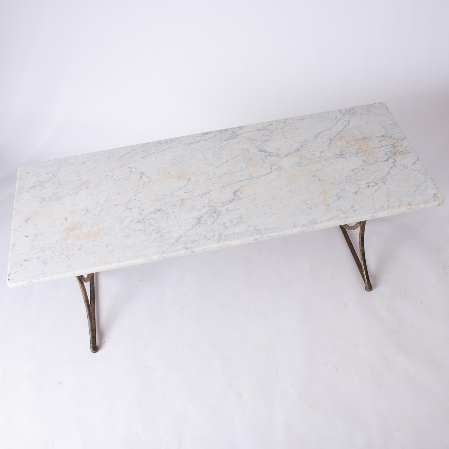 This table has a wonderful antique white marble top that is almost one inch thick. The base, made of handwrought iron, has a very sleek and unusual design with a surface that shows traces of old bronze paint. The marble top shows some discolorations