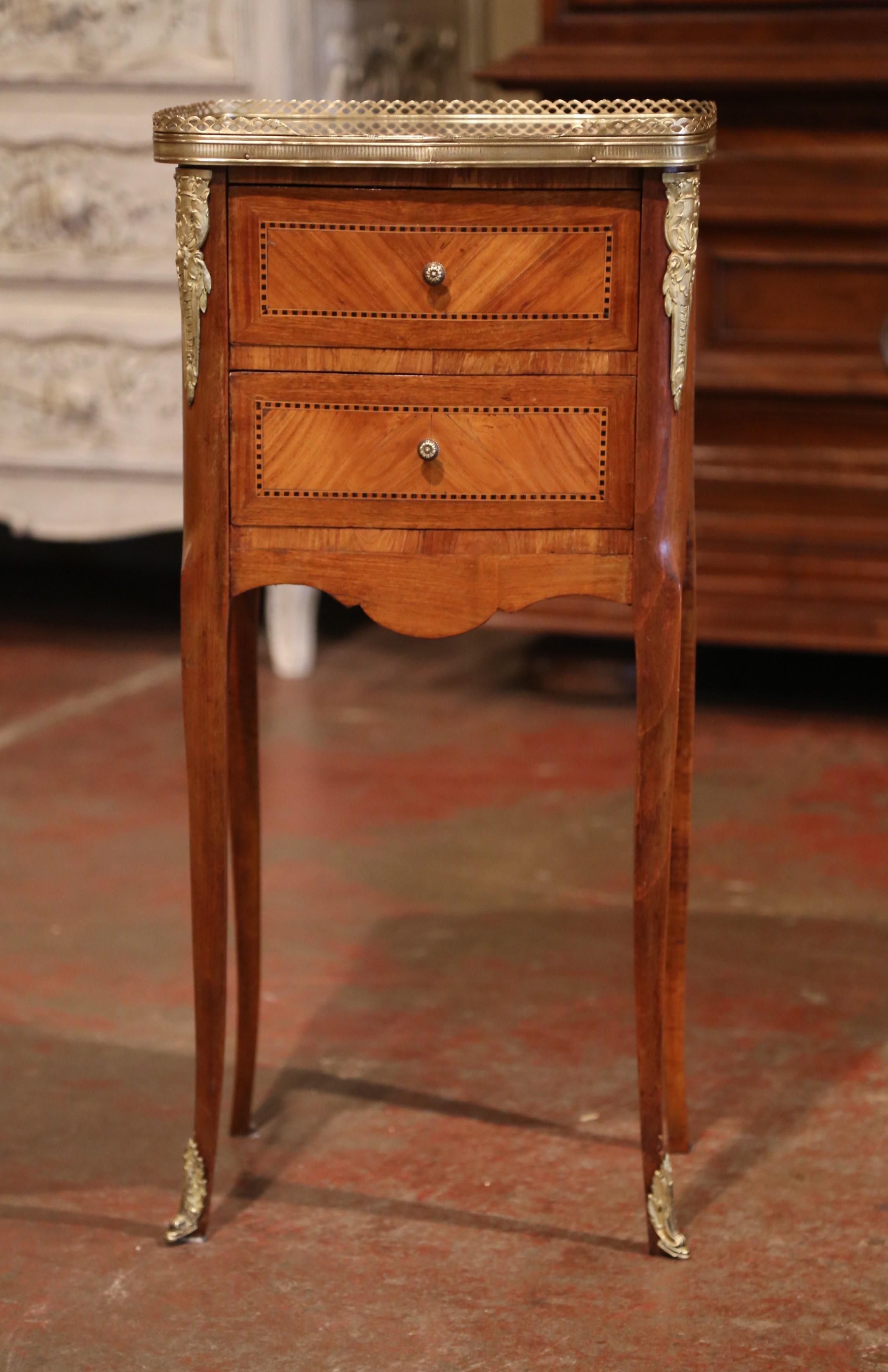 Crafted in France circa 1890, this elegant antique chest sits on cabriole legs decorated with bronze caps feet over a scalloped apron. The petite Louis XV style commode features two drawers across the front decorated with marquetry inlay work and