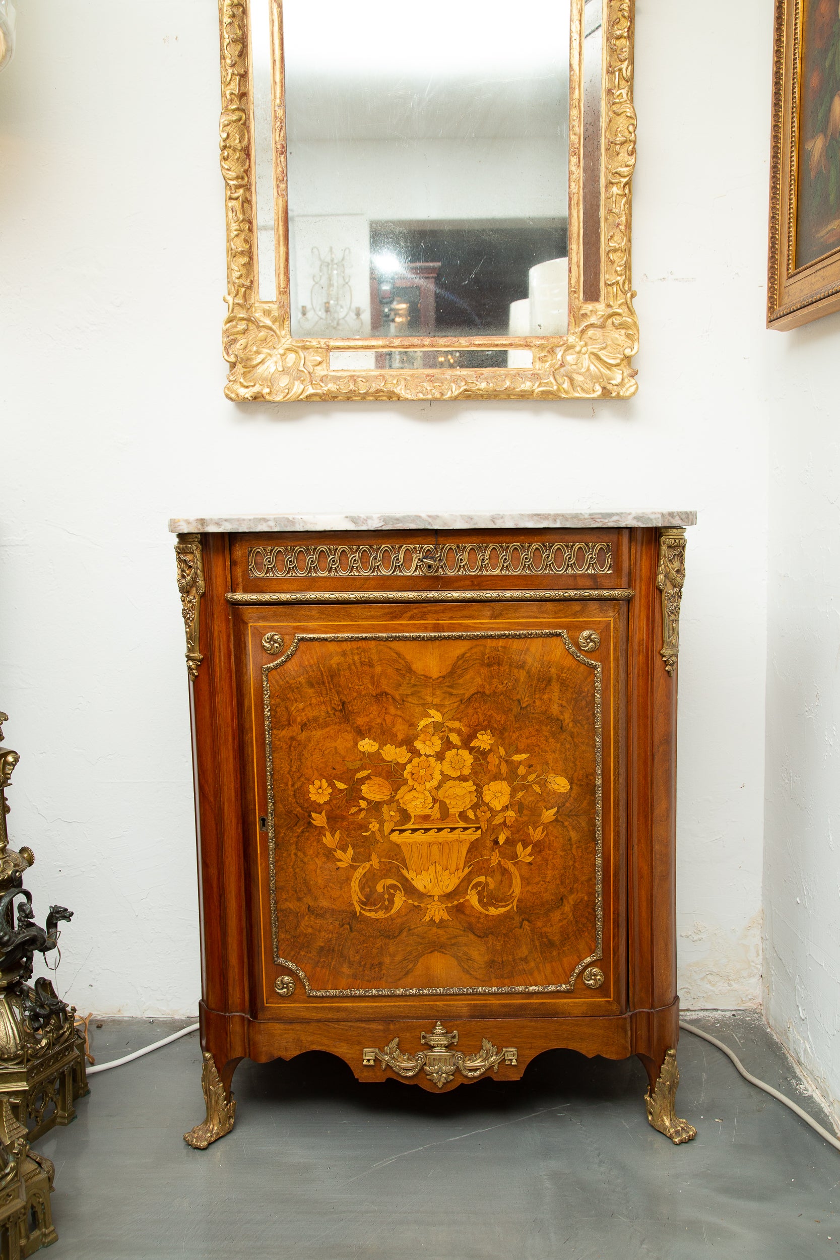 This is an elegant Louis XV style walnut cabinet. The gray variegated marble top rests over a single door with satinwood marquetry in the form of a floral arrangement in an urn. The cabinet has a beautifully shaped apron flanked by gilt metal paw