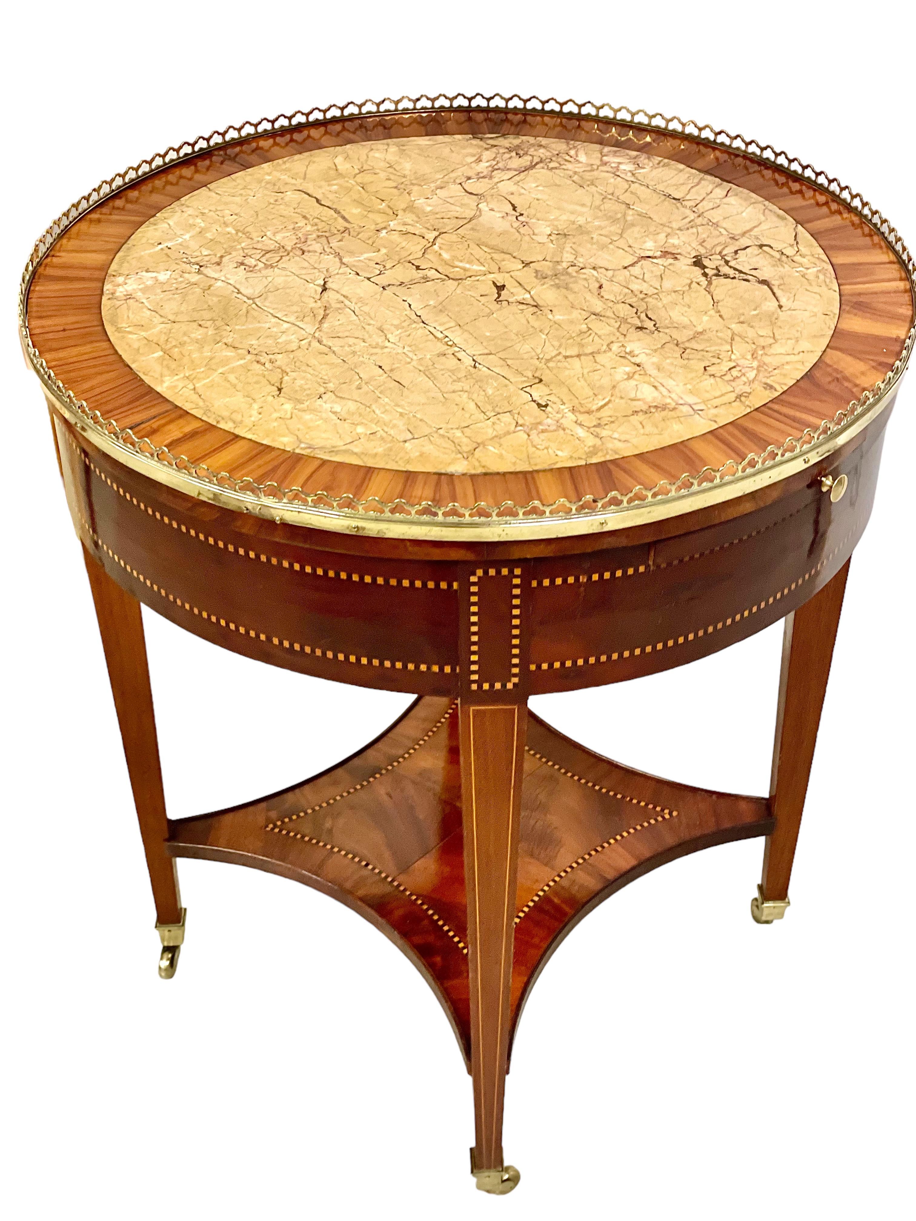A fine French Louis XVI style 'Bouillotte' table, in wood veneer and marquetry, with an inlaid beige veined marble top surrounded by an openwork brass gallery. The gambling card game of bouillotte was so popular in France during the 18th century