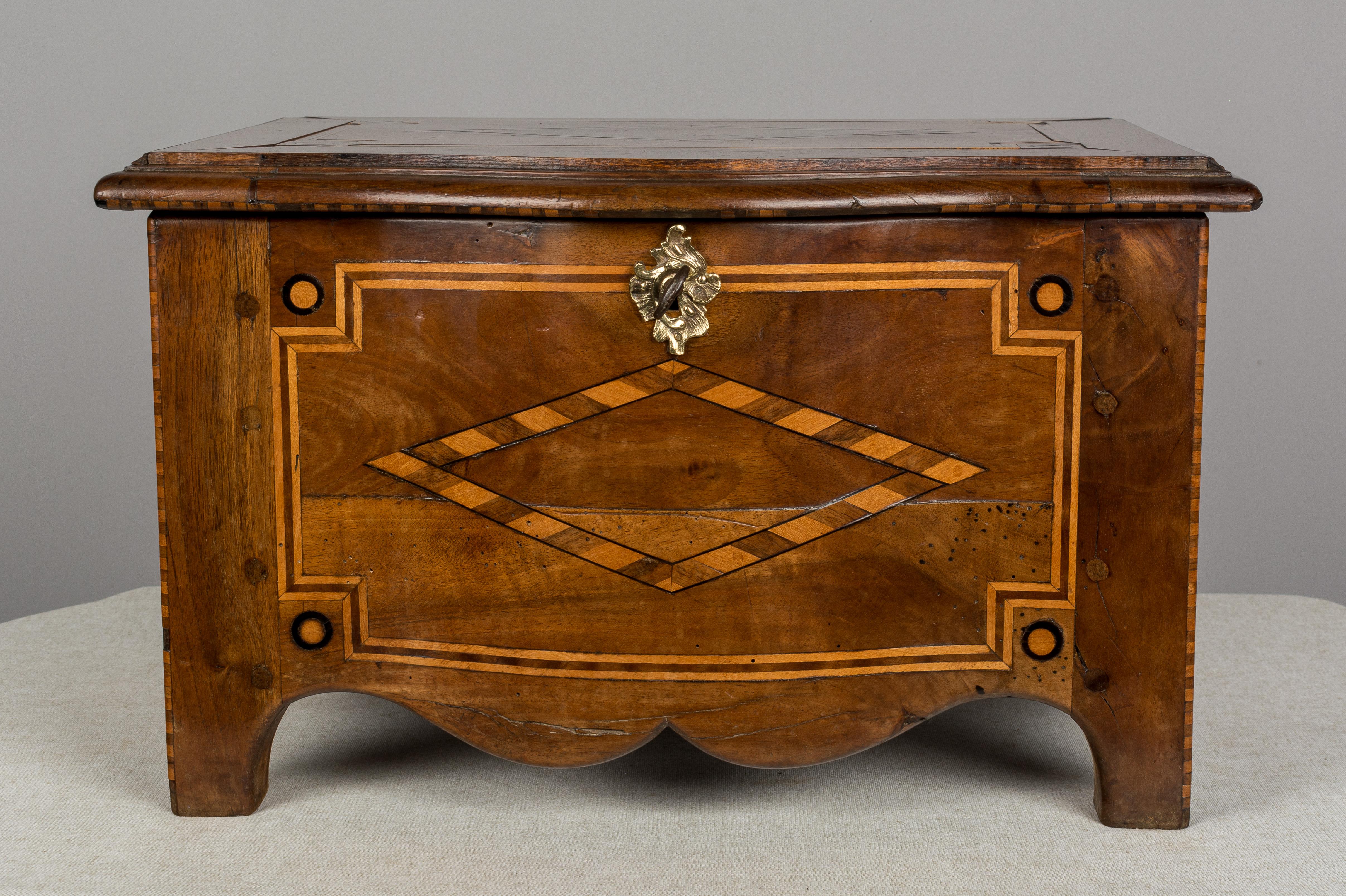 An early 19th century miniature French coffer, or small hinged box, made of solid walnut with marquetry inlay. Original decorative bronze hardware and large iron hinges. Working lock and key. Three stacking trays for storing silverware were