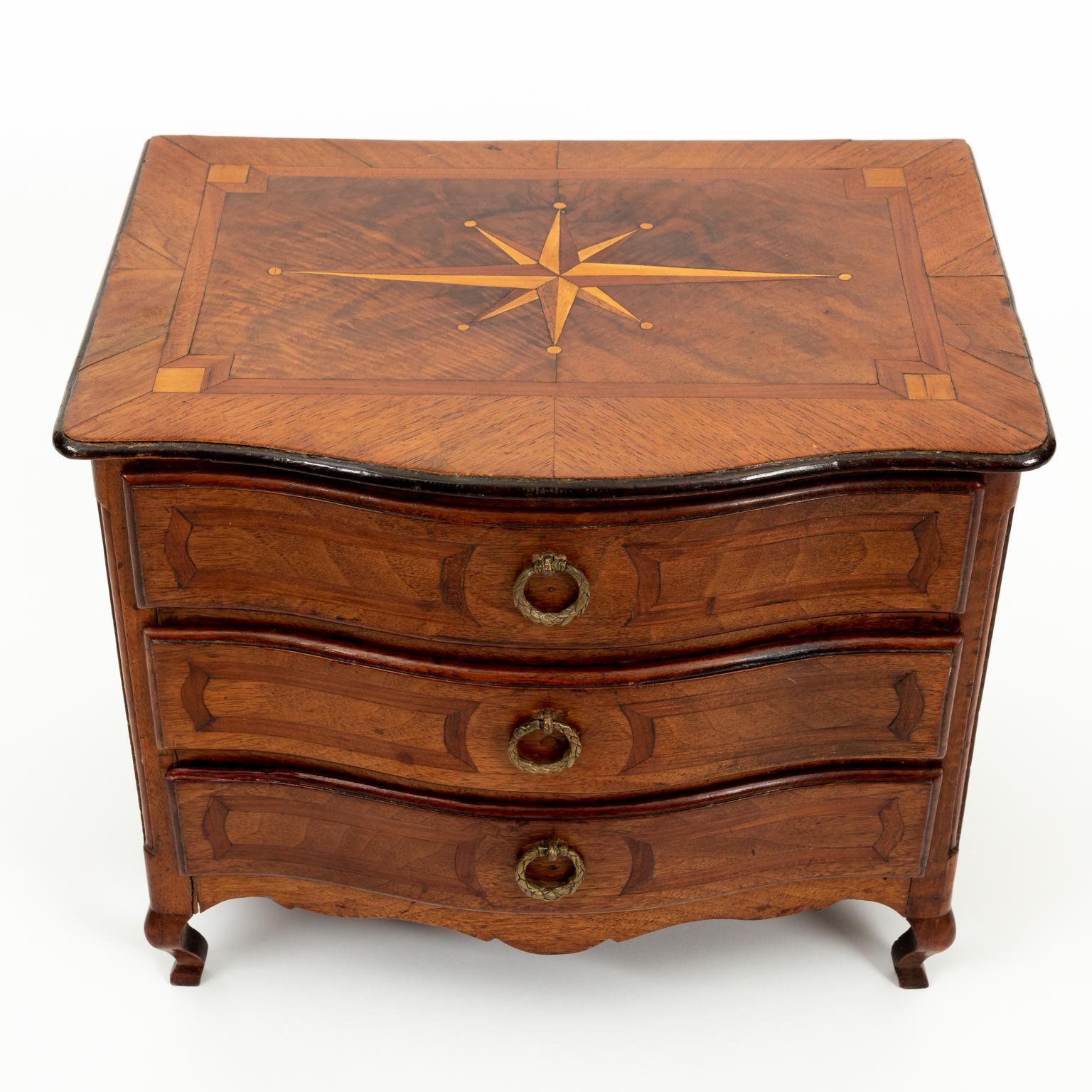 Circa 1860s 19th century French marquetry miniature chest of drawers with bronze handles and inlaid starburst design on the tabletop. Made in France. Please note of wear consistent with age including minor repair on upper lip of bottom drawer. Minor