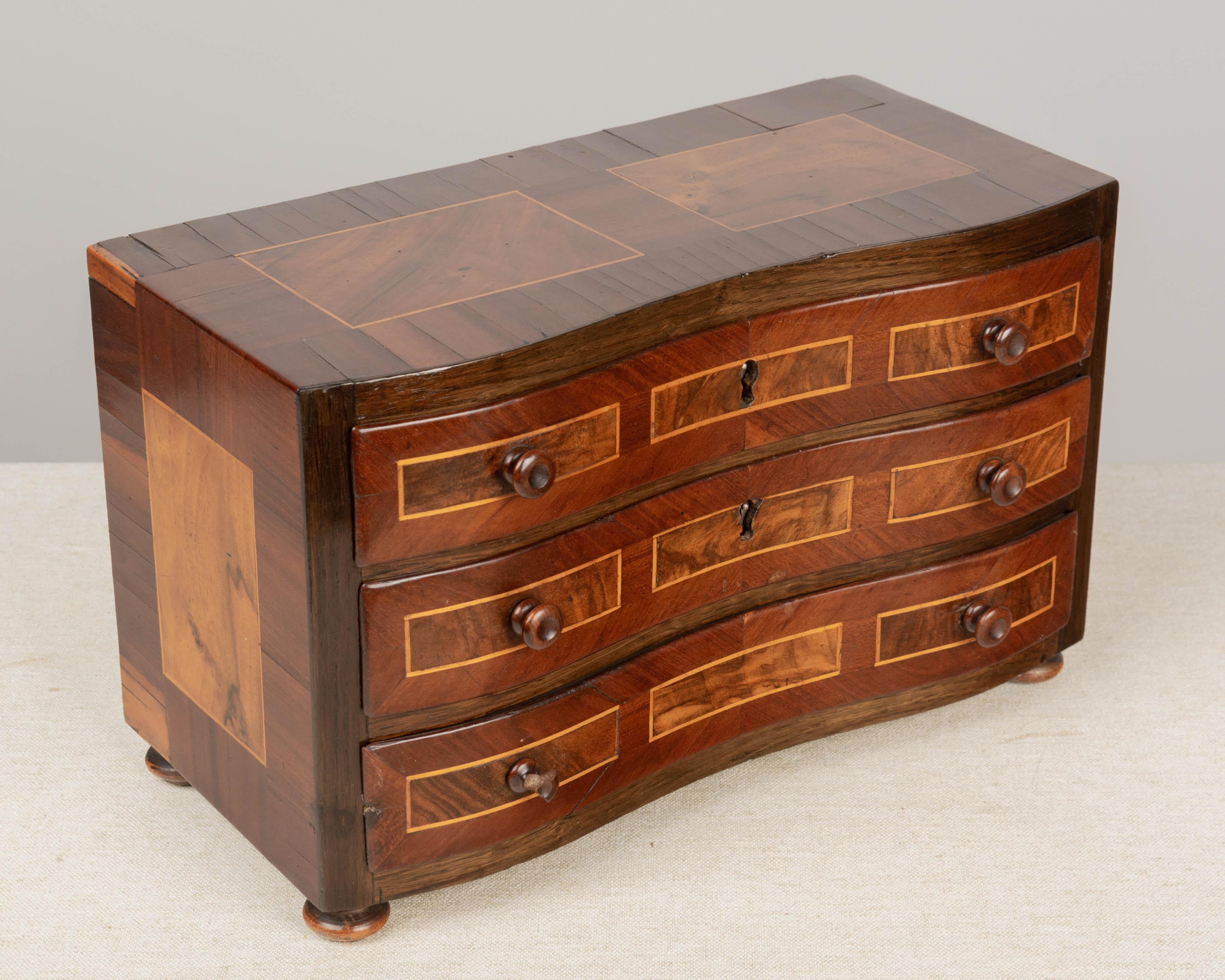 A 19th century French marquetry commode de maitrise, or miniature sample commode with serpentine front. Fine inlaid veneers of mahogany and walnut. Three dovetailed drawers with turned knobs. Mortise and tenon construction. Small loss to bottom left