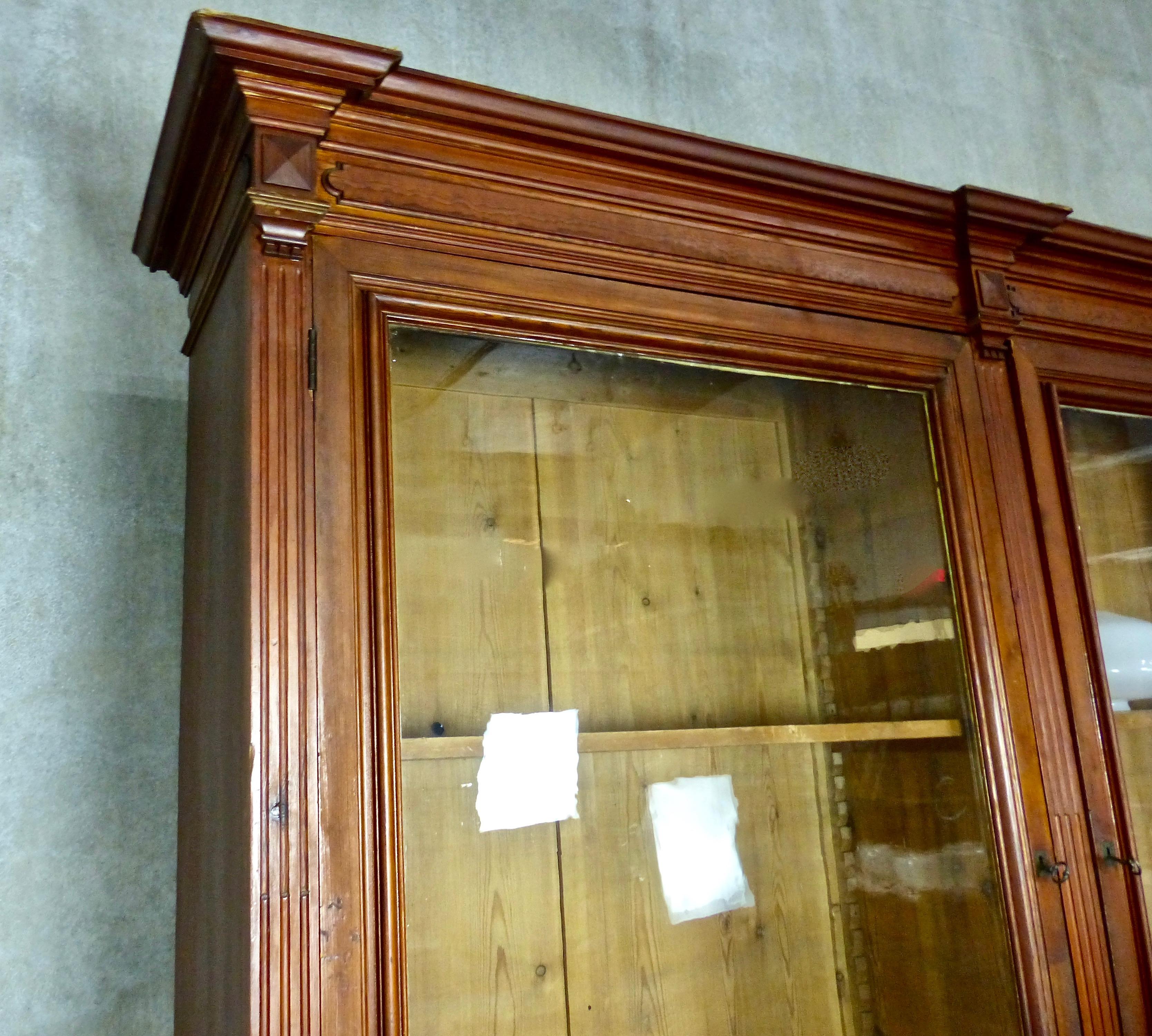 A substantial (8 x 11 foot) French display cabinet that comes in two distinct sections — an upper, recessed cabinet with shelves and glass doors, and a table-like base with eight turned-wood legs. Plenty of elegant, handcrafted details in its