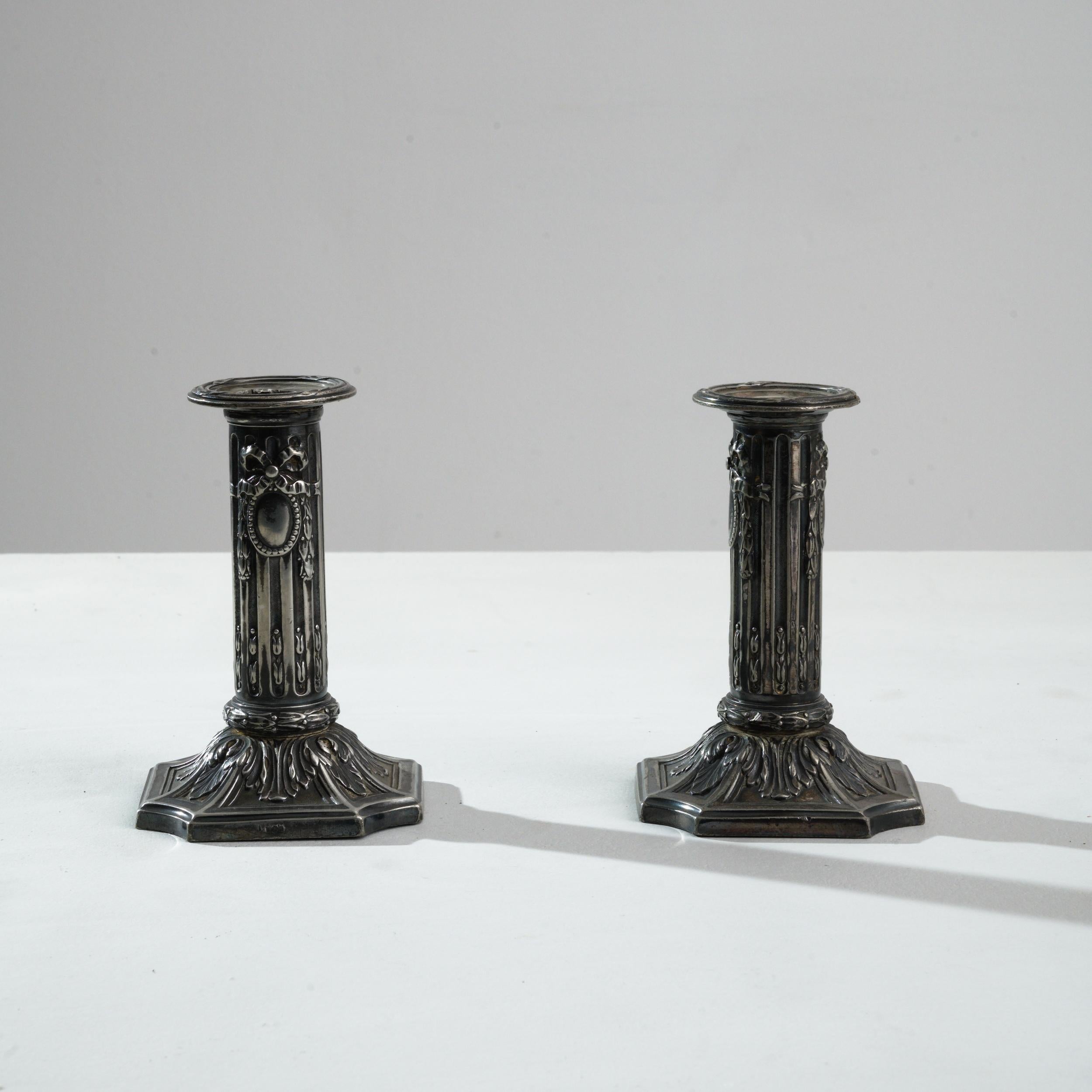 A pair of metal candlesticks created in 19th century France. This pair of cast metal candlesticks exude a regal and distinguished air, wearing each a proud coat of arms scrupulously carved into their columns and scroll patterning described across