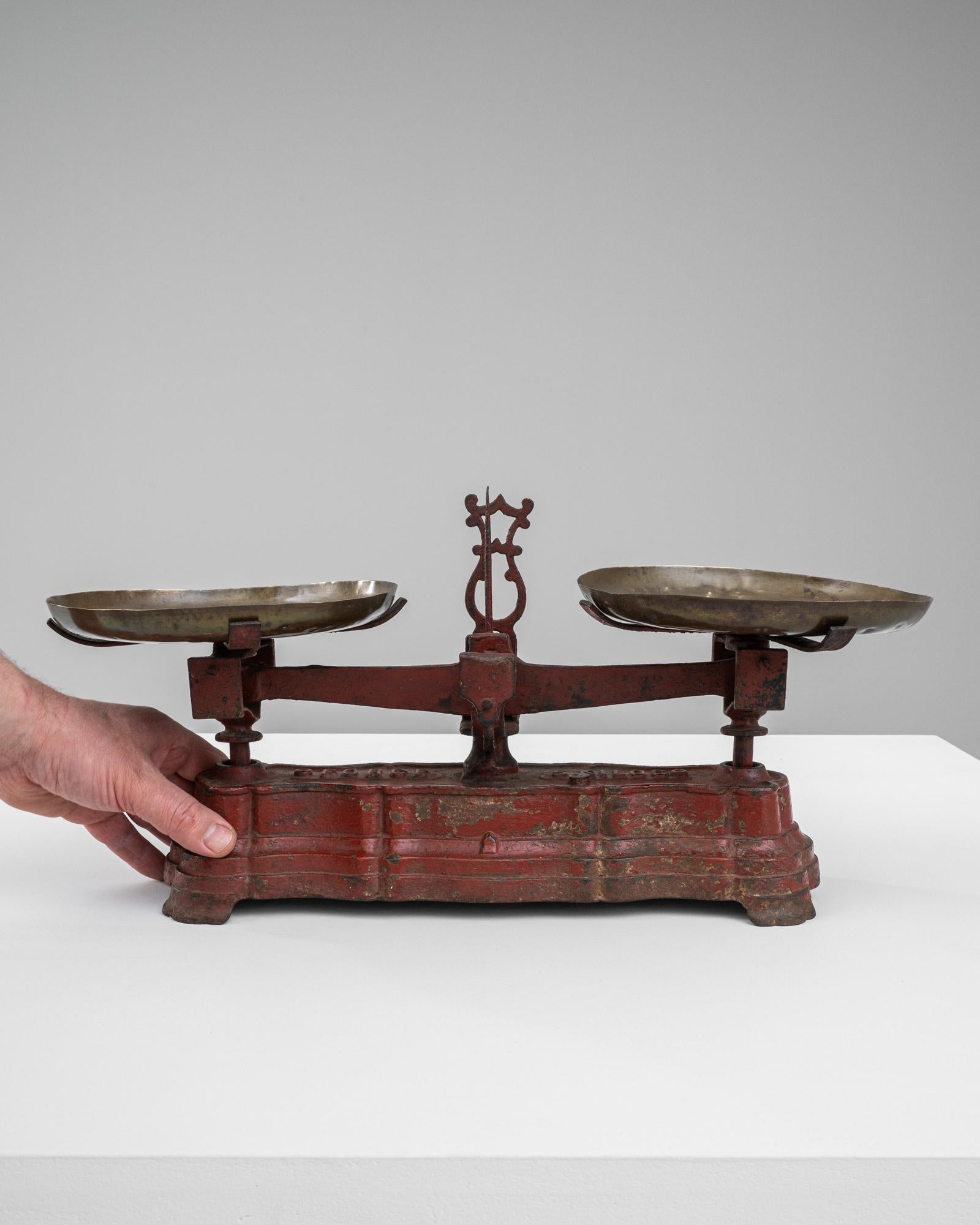 This 19th Century French Metal Scale is a striking artifact that captures the essence of historical commerce and French provincial life. Clad in its original red paint, now distressed with time, it speaks to its years of service and the hands it has