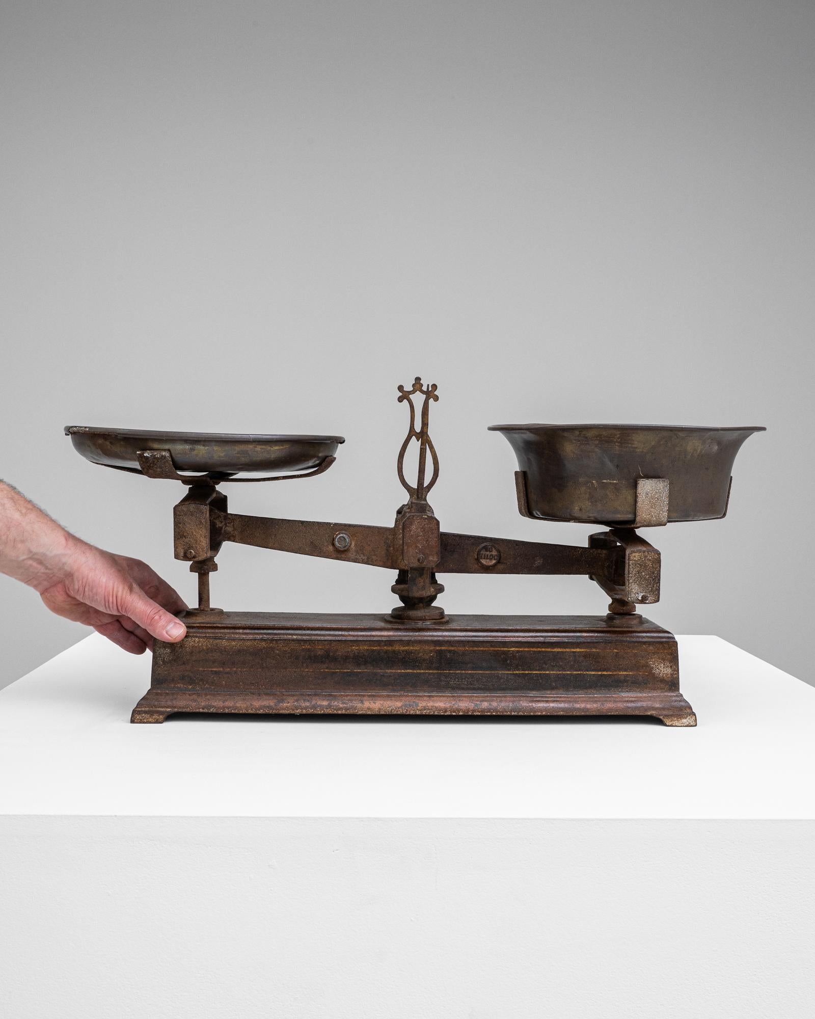 This distinguished 19th Century French Metal Scale is an emblem of the rich historical past, resonating with the tales of traditional marketplaces where it once played a pivotal role. The scale, with its robust wooden base and weathered metal bowls,