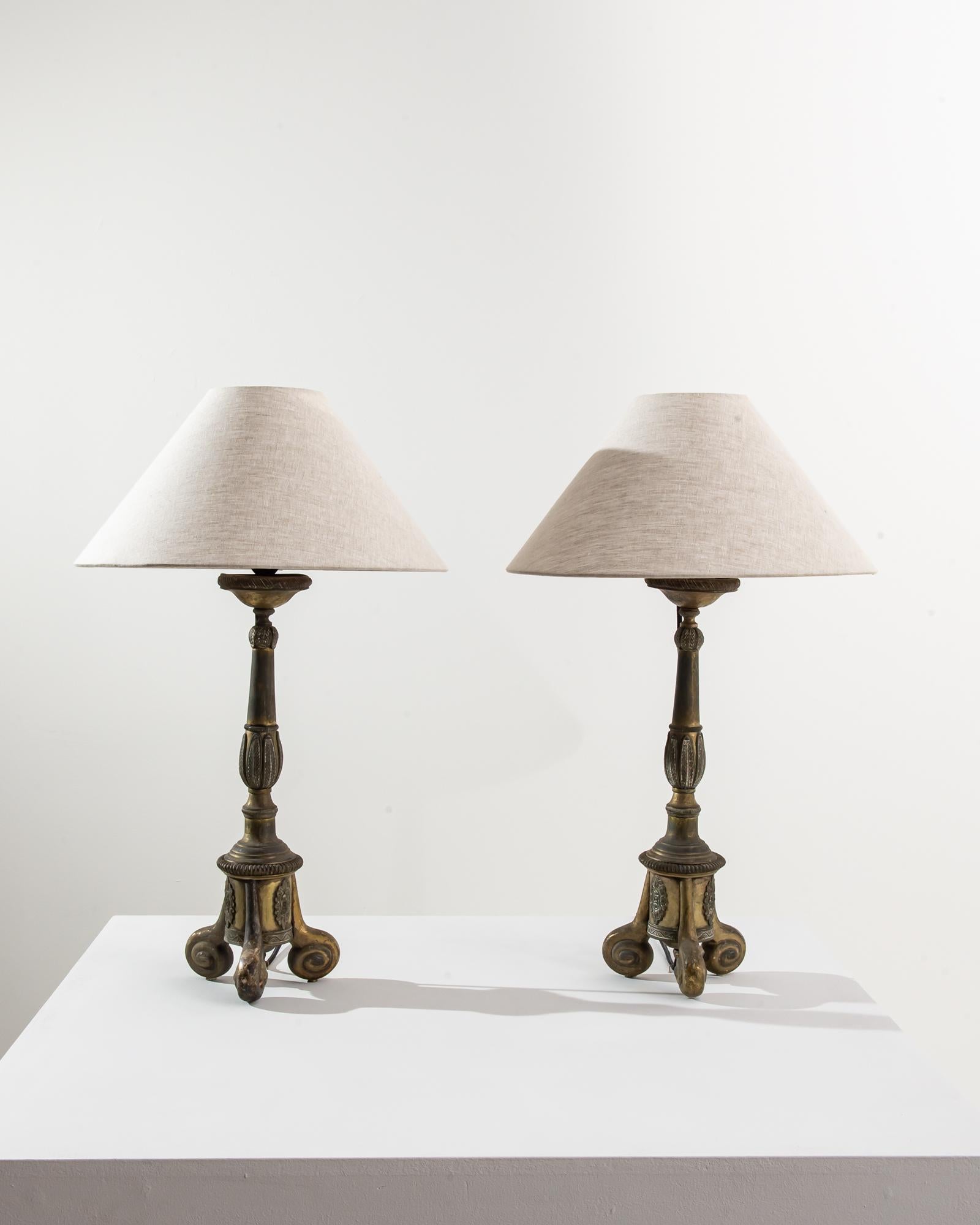 A pair of 19th century metal table lamps produced in France, standing on small shell tripod feet. The ornate shaft is adorned with daintily carved indents and leaves, completed by an intricate floral gadroon and frieze at its base. Lending a soft