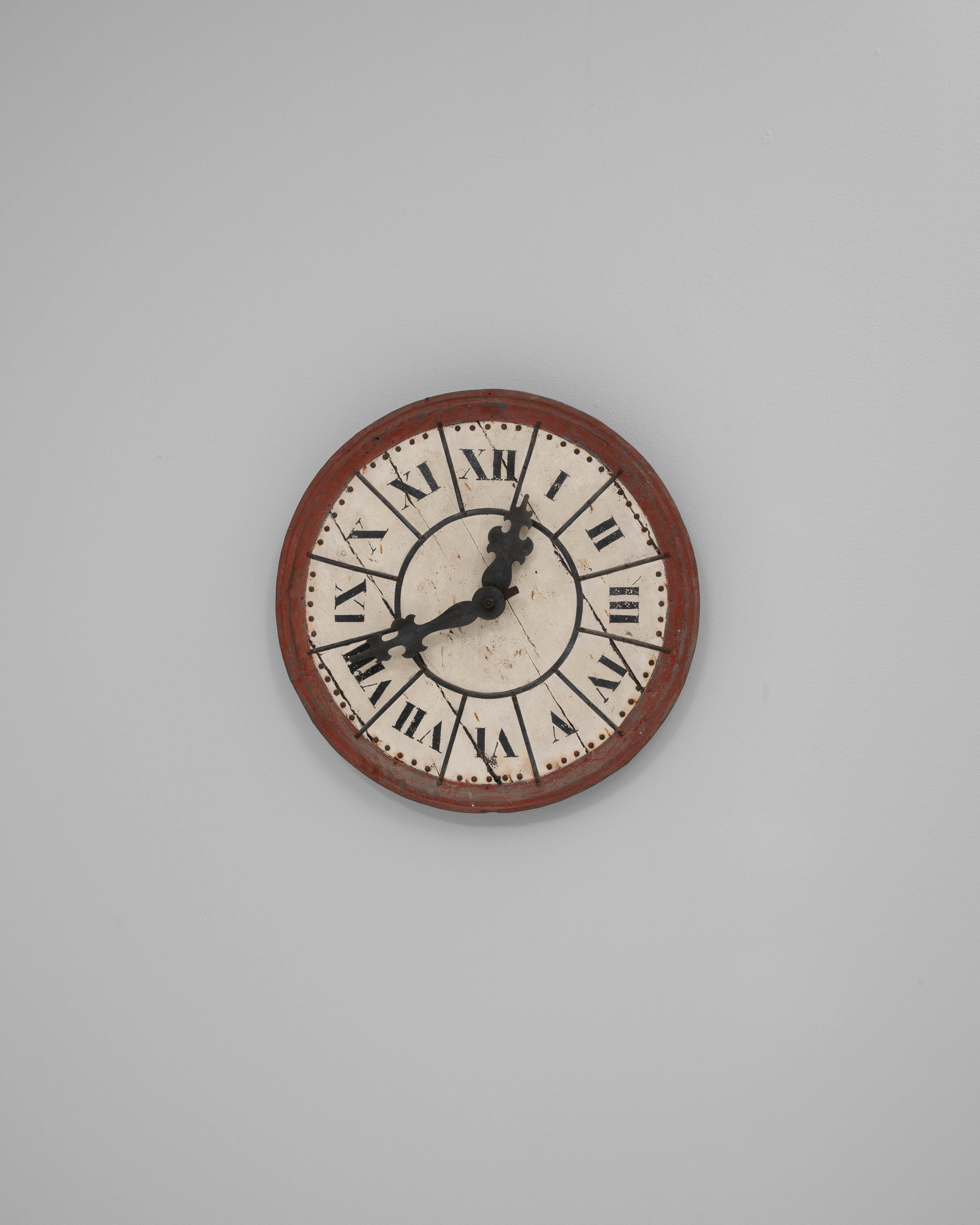 This 19th Century French wall clock is a bold decorative piece combining rustic charm with graphic impact. The circular face features large Roman numerals hand-painted on a weathered metal surface, framed by a deep red wooden border that enhances