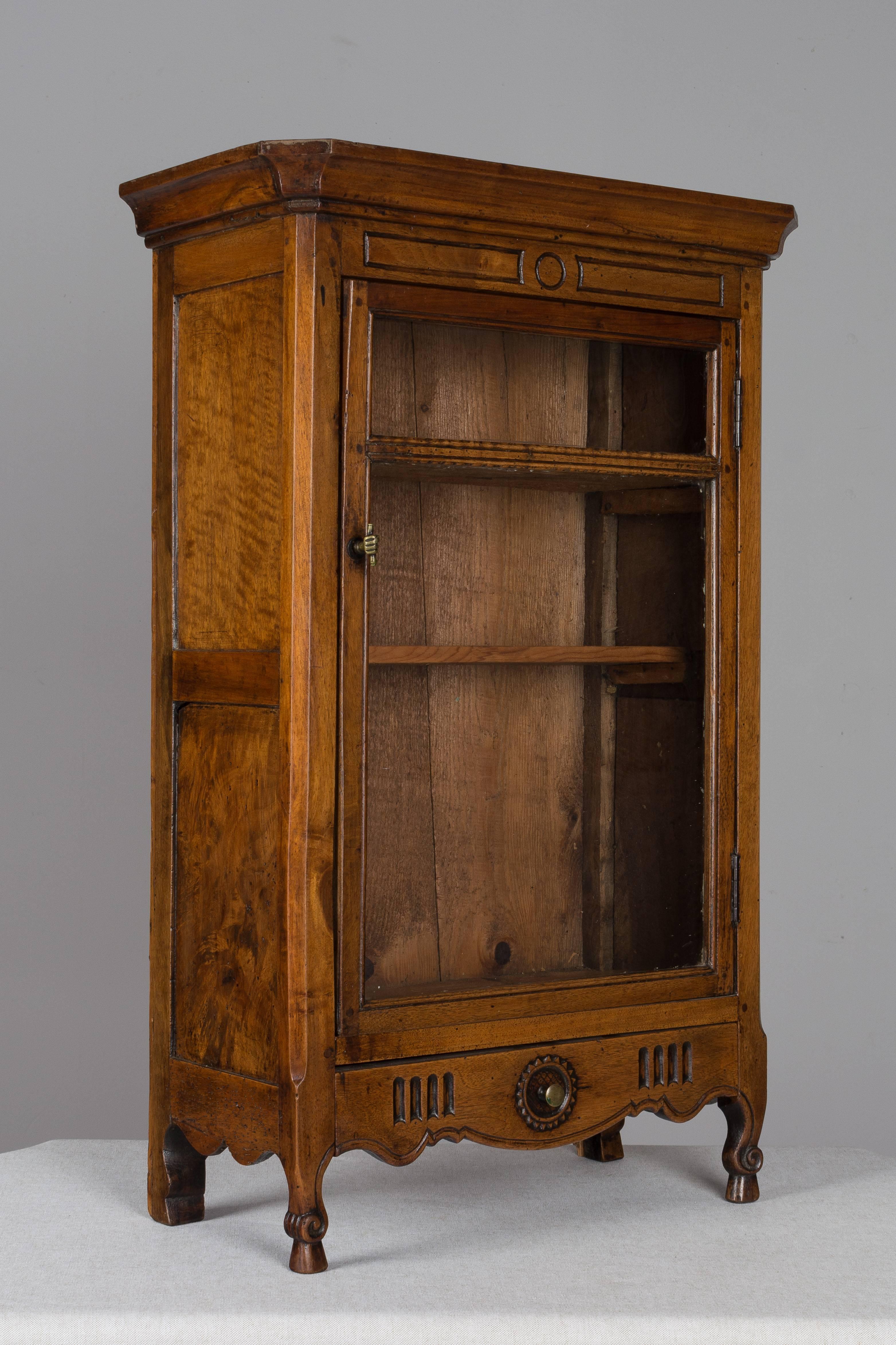 From the South of France, this 19th c. verrio is made of solid walnut with a two panel glass door having the original panes. Scalloped drawer with simple carved sunflower surrounding the small brass knob. Two front scroll legs. Mortise and tenon and