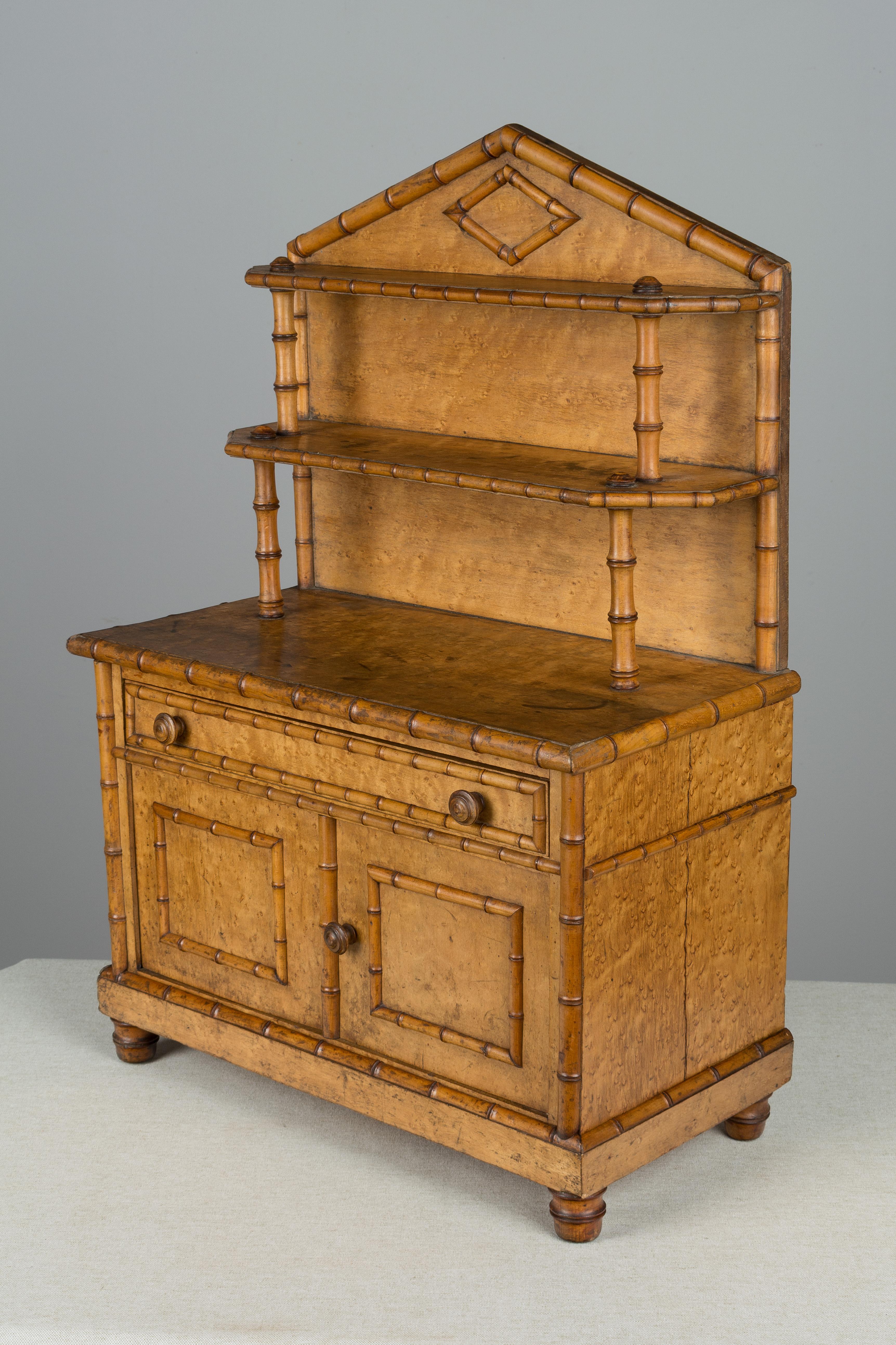 A 19th century French miniature faux bamboo buffet made of bird’s eye maple. Well-crafted with tiered shelves on top and cabinet doors opening to a single shelf. A unique large scale doll furniture piece. Left back foot is missing, as found.