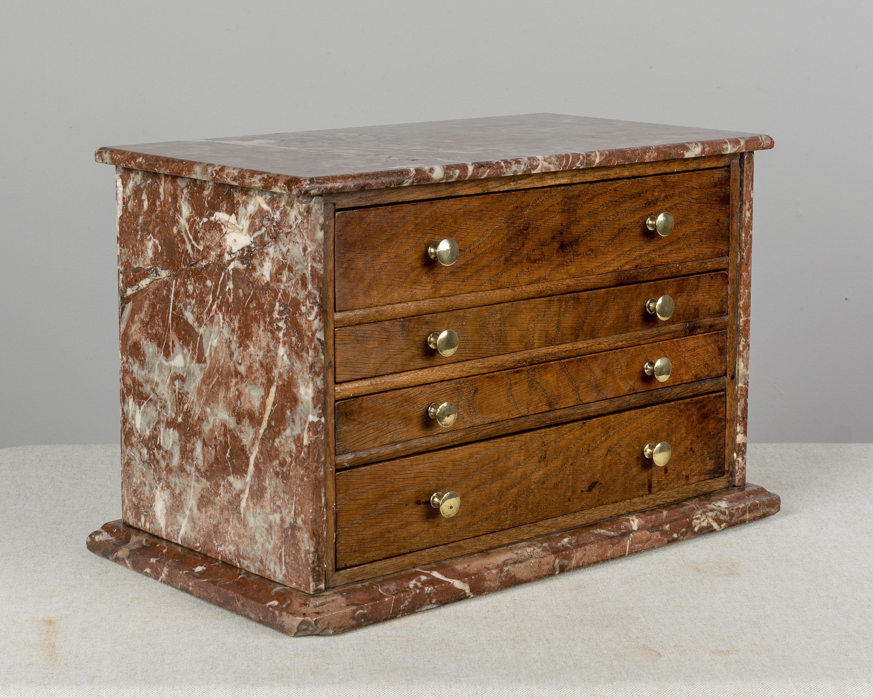 An unusual 19th century French miniature chest clad in Rouge Royal marble. Four dovetailed drawers are made of oakwood on the face and have polished brass knobs. The bottom drawer is divided.  Pine as a secondary wood. All original. Perfect for