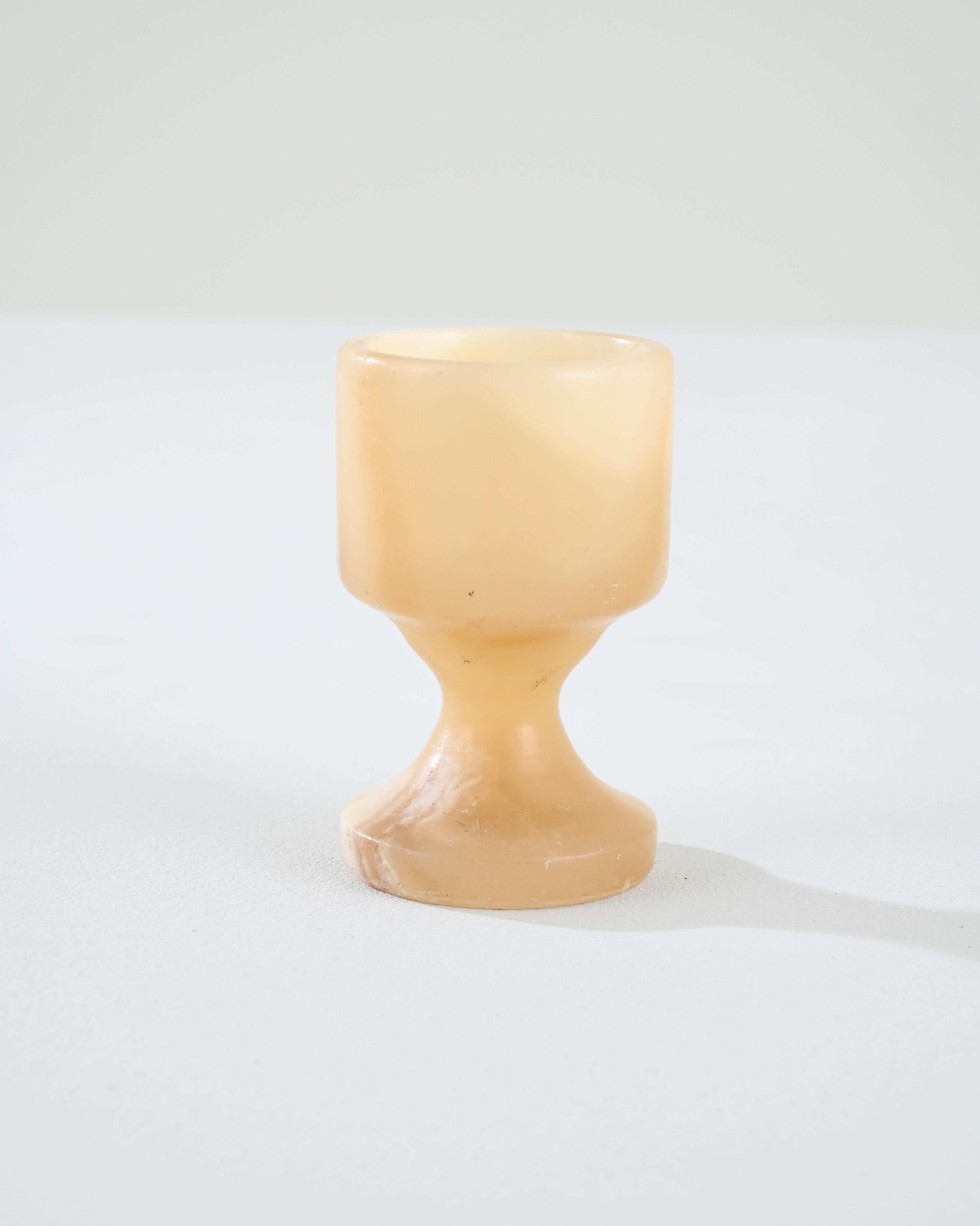 A marble chalice made in 19th century France. This petite drinking glass displays a bright and sunny disposition, crafted with simple yet refined artisanal expertise. Veins of darker details run diagonally across the sandy-beige marble, creating an