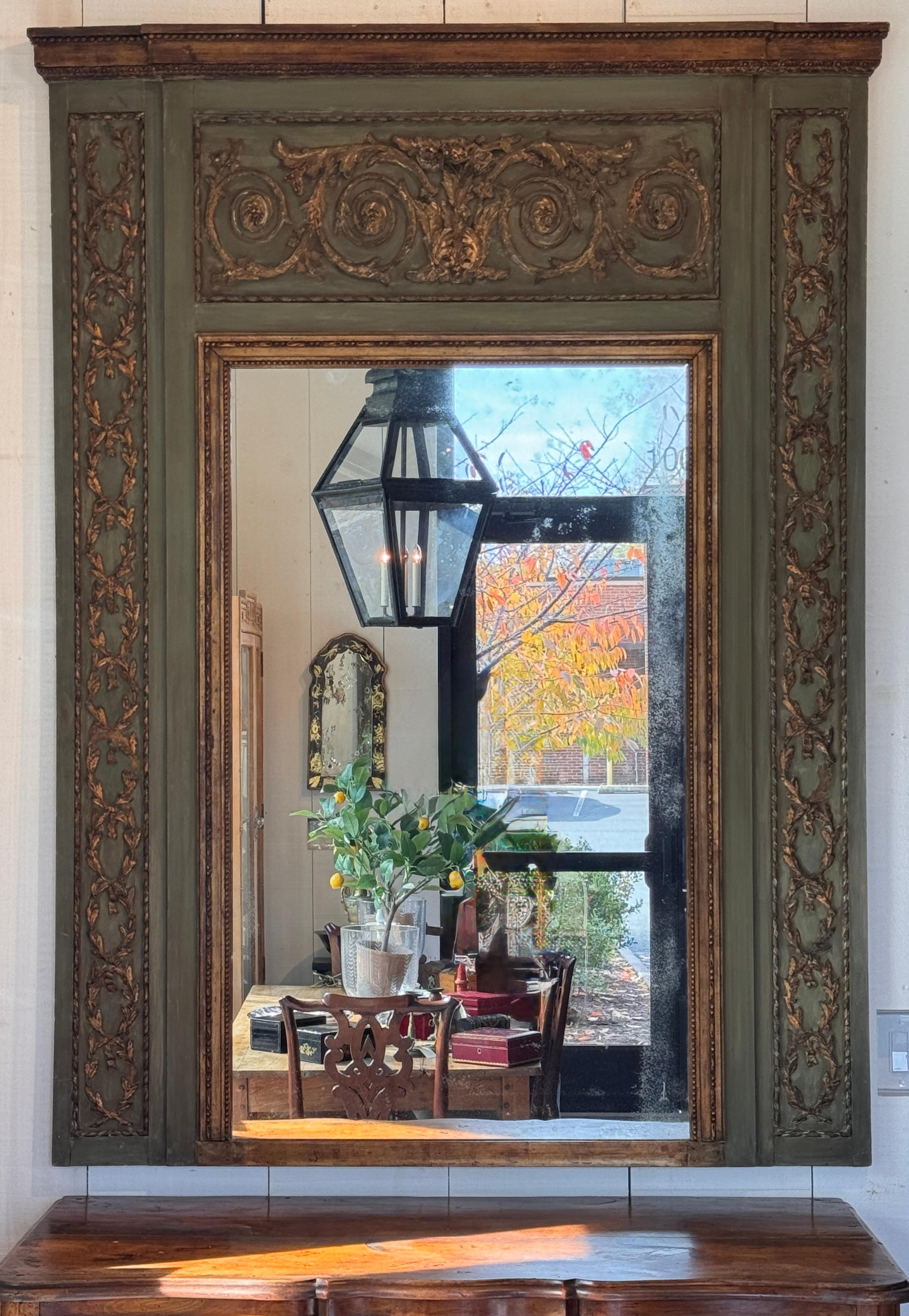 Specchio francese del XIX secolo con volute intagliate e dorate su una cornice dipinta di verde tenue. Lo specchio presenta intricati dettagli neoclassici con motivi di alloro e acanto e conserva una superficie invecchiata e morbidamente patinata.