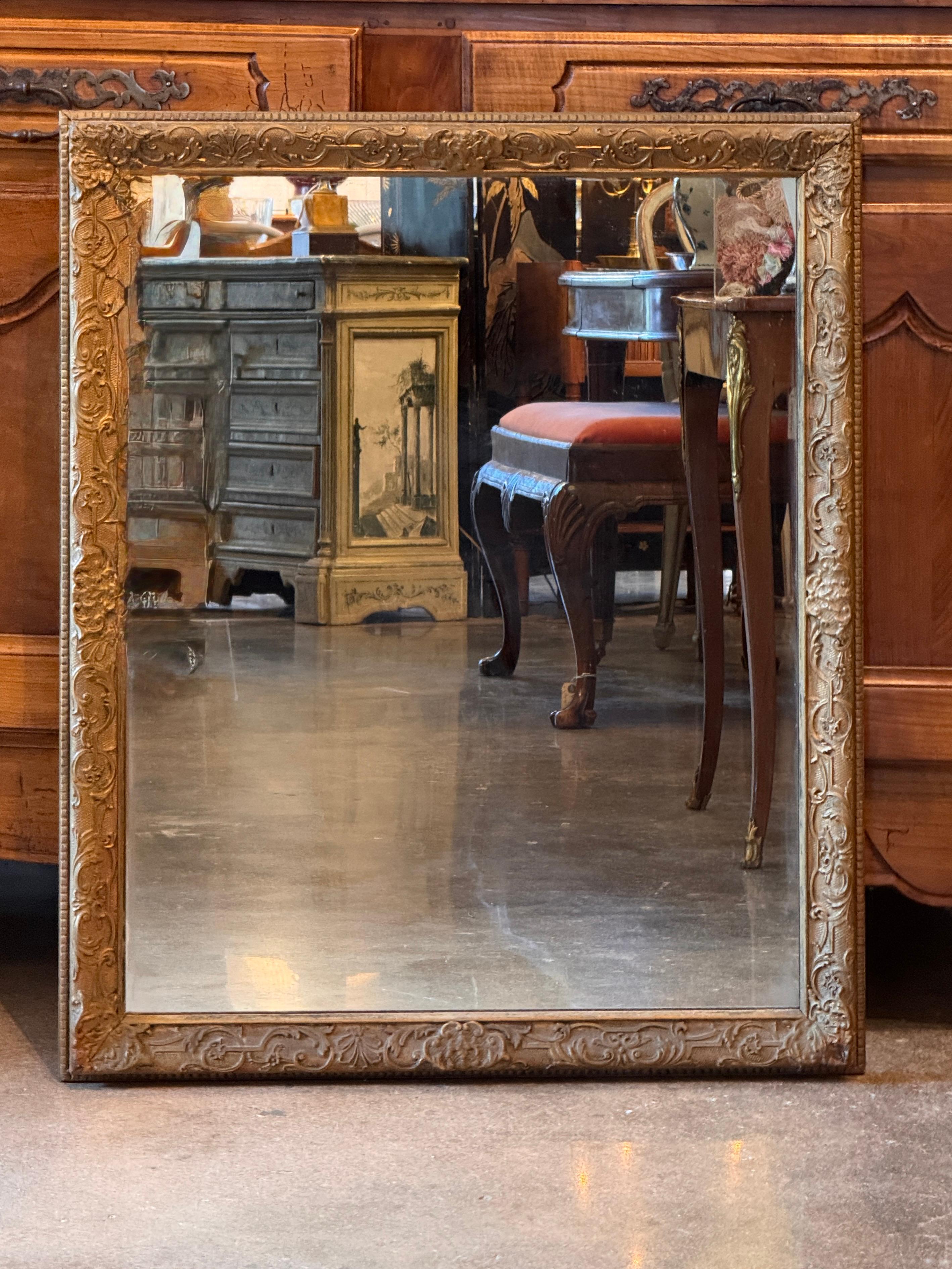 Miroir français dans un cadre en bois doré avec des motifs de feuillage et de coquillages en relief dans les coins et sur les bords. La surface présente une patine douce, mettant en valeur les détails de la sculpture et l'ancienneté de la pièce.
