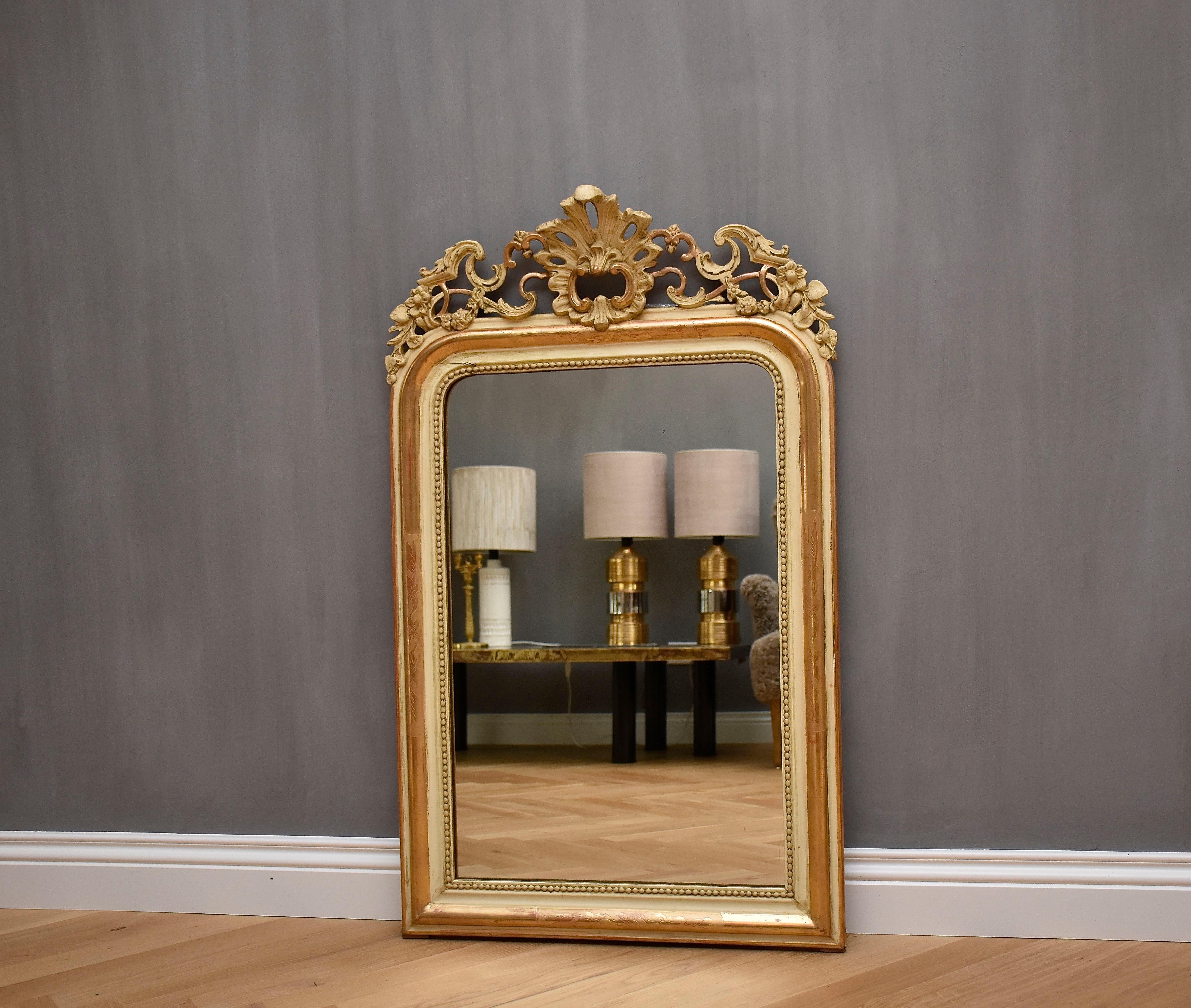 Magnifique miroir français ancien avec une fabuleuse crête et une vitre d'origine légèrement roussie.
Le cimier est orné d'une décoration florale et de C-scrolls.
Le cadre est de couleur blanc cassé, doré à la feuille d'or et doté d'un bord