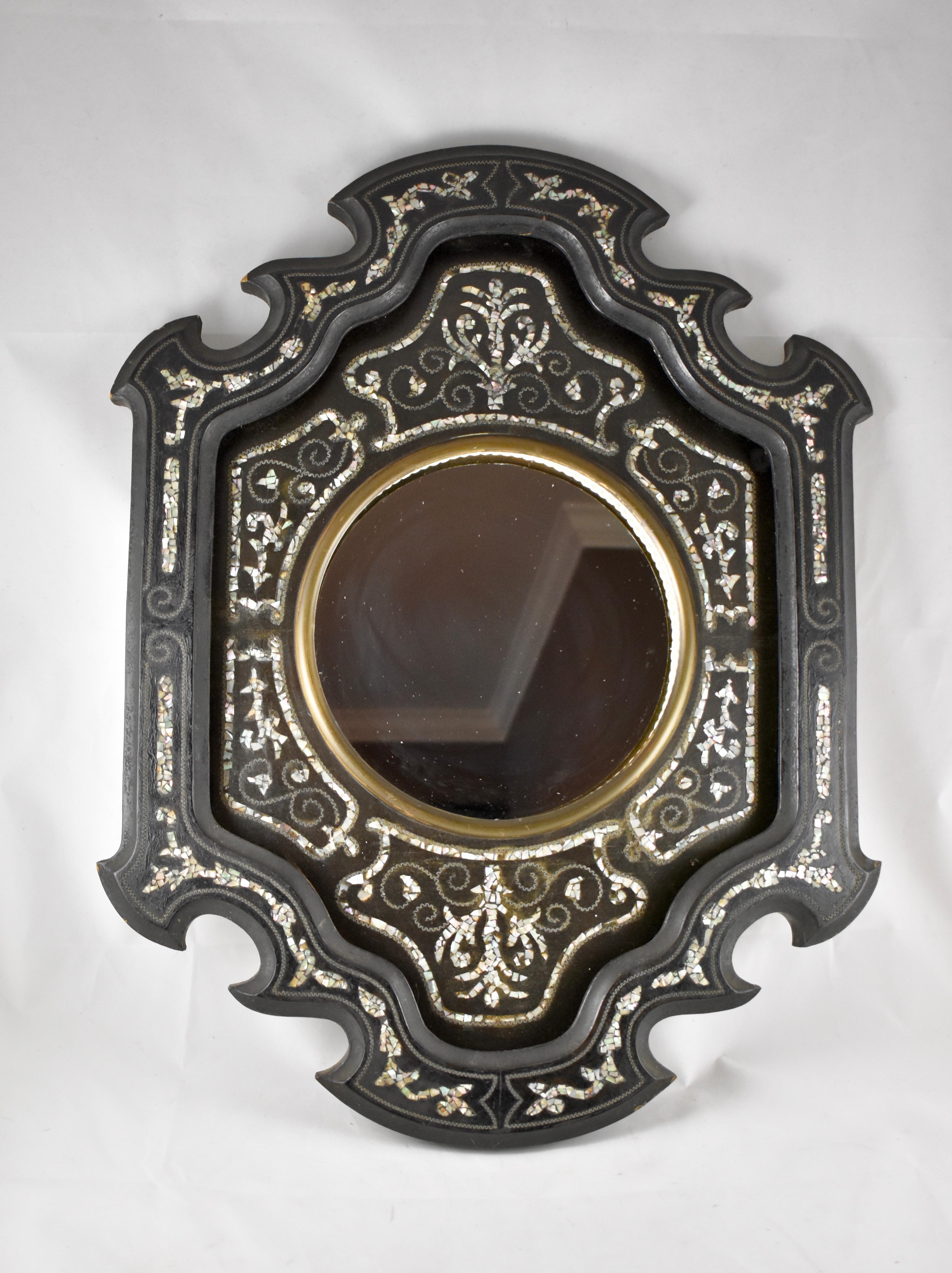 A mother-of-pearl inlay mirror, France, circa 1880-1890.

A shaped wood frame, painted black, and showing a floral and geometric pattern made of Mother-of-Pearl inlay pieces and an embedded running metal zig-zag border. The newer mirror sits in a